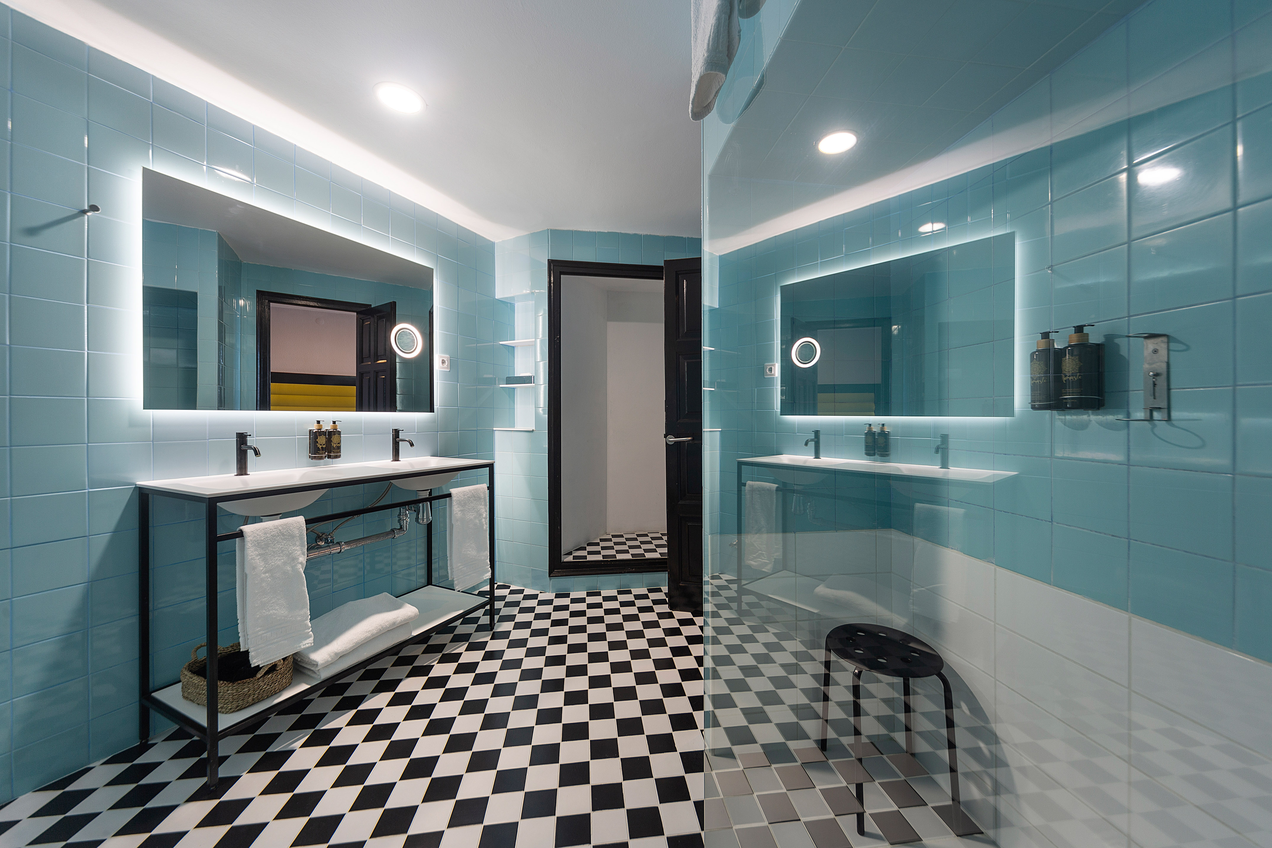 Modern blue bathroom with checkered floor, double vanity, backlit mirrors.