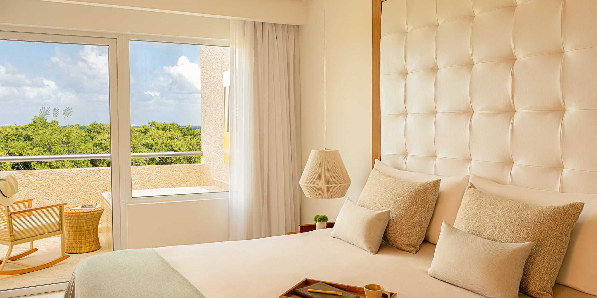 Resort bedroom with tufted king bed, balcony, tropical ocean view.
