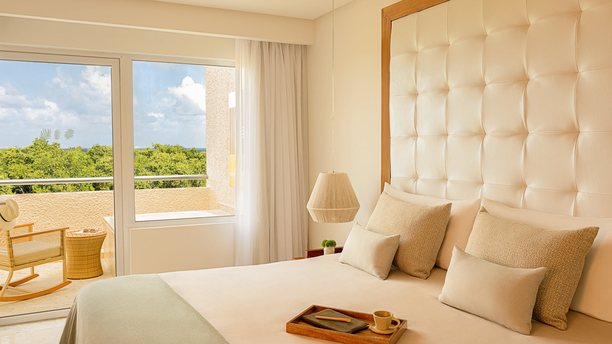 Resort bedroom with tufted king bed, balcony, tropical ocean view.