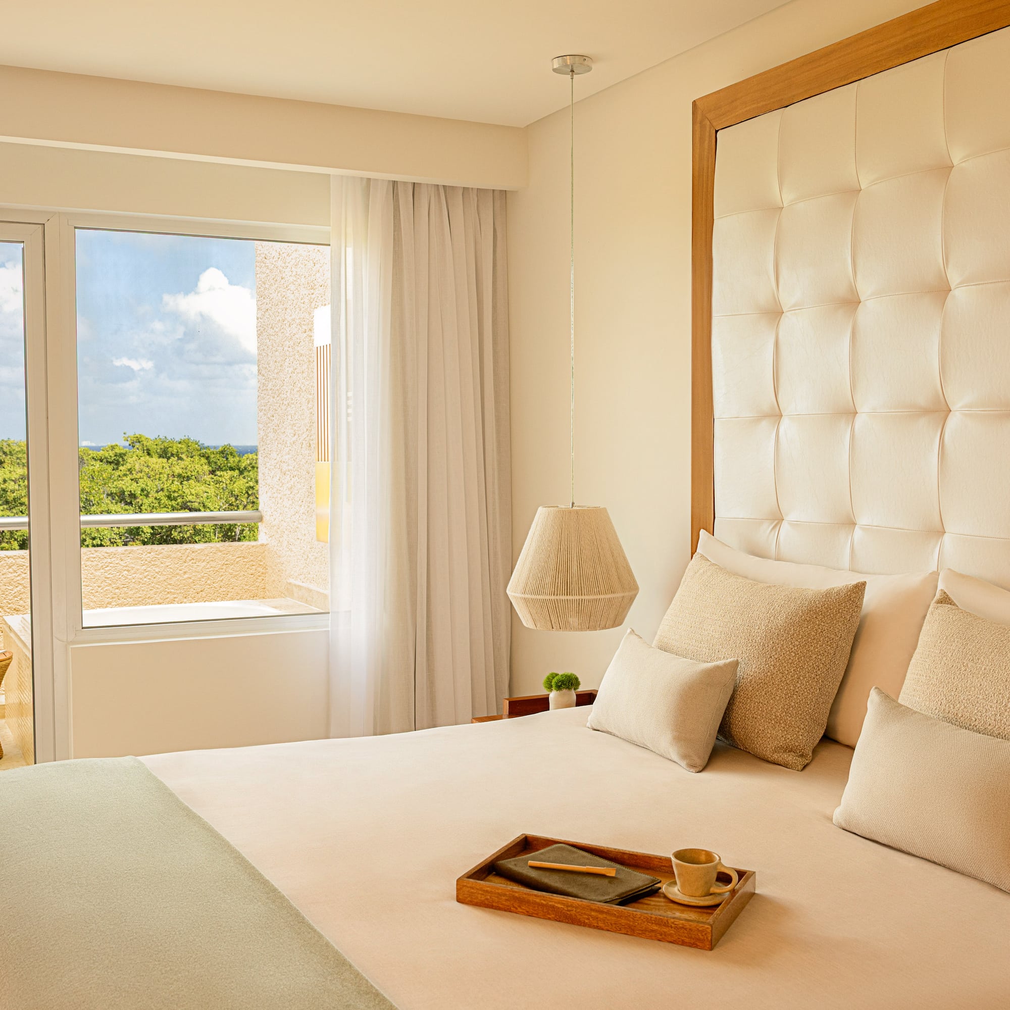 Resort bedroom with tufted king bed, balcony, tropical ocean view.