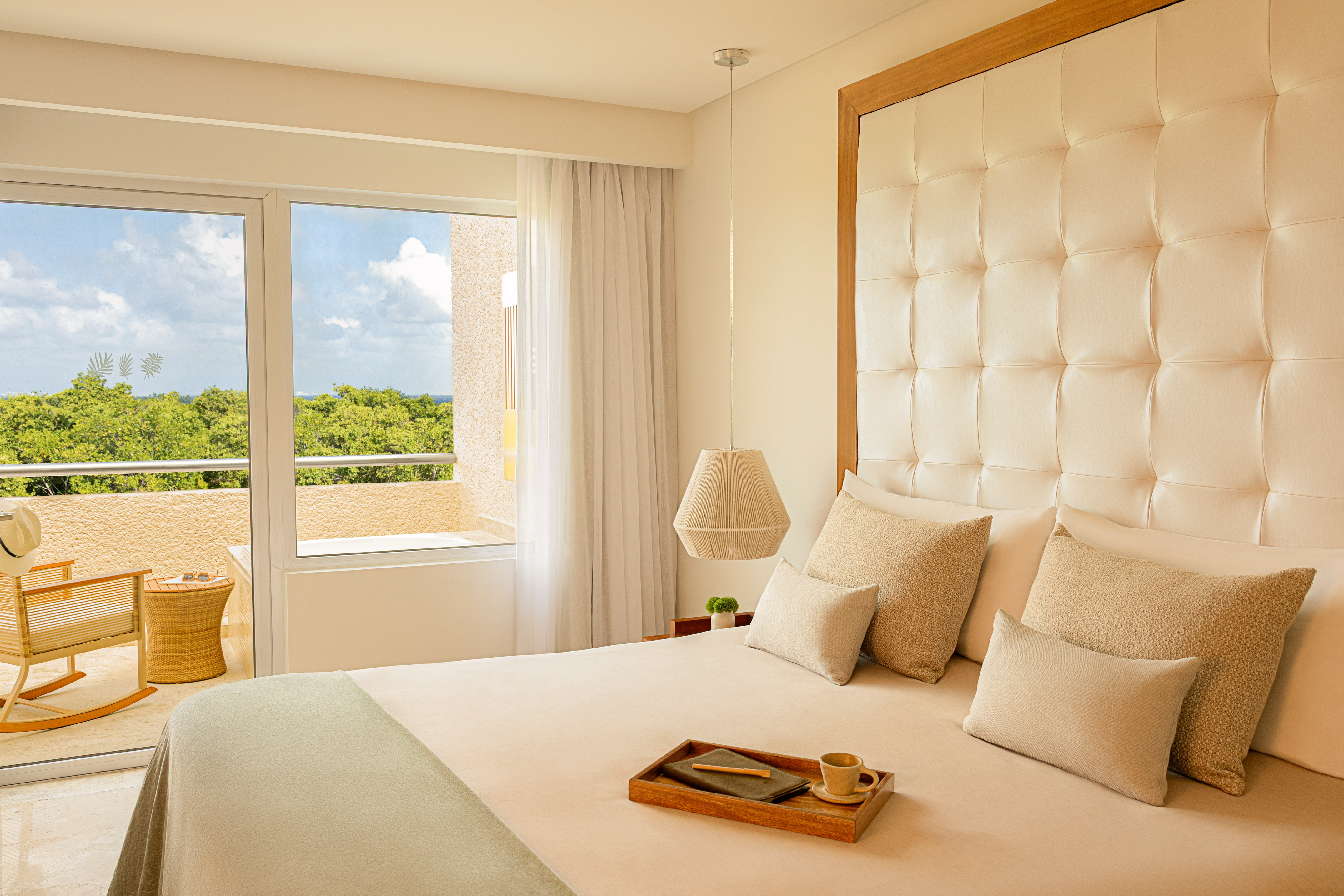 Resort bedroom with tufted king bed, balcony, tropical ocean view.