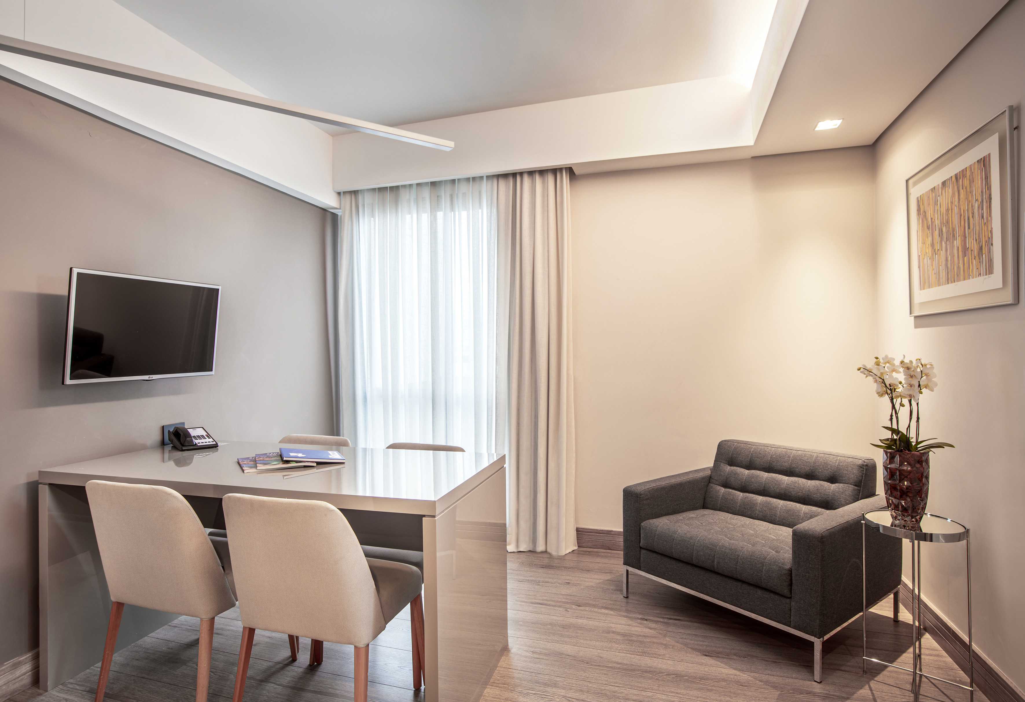 Modern office with sleek desk, chairs, wall TV, and gray armchair.
