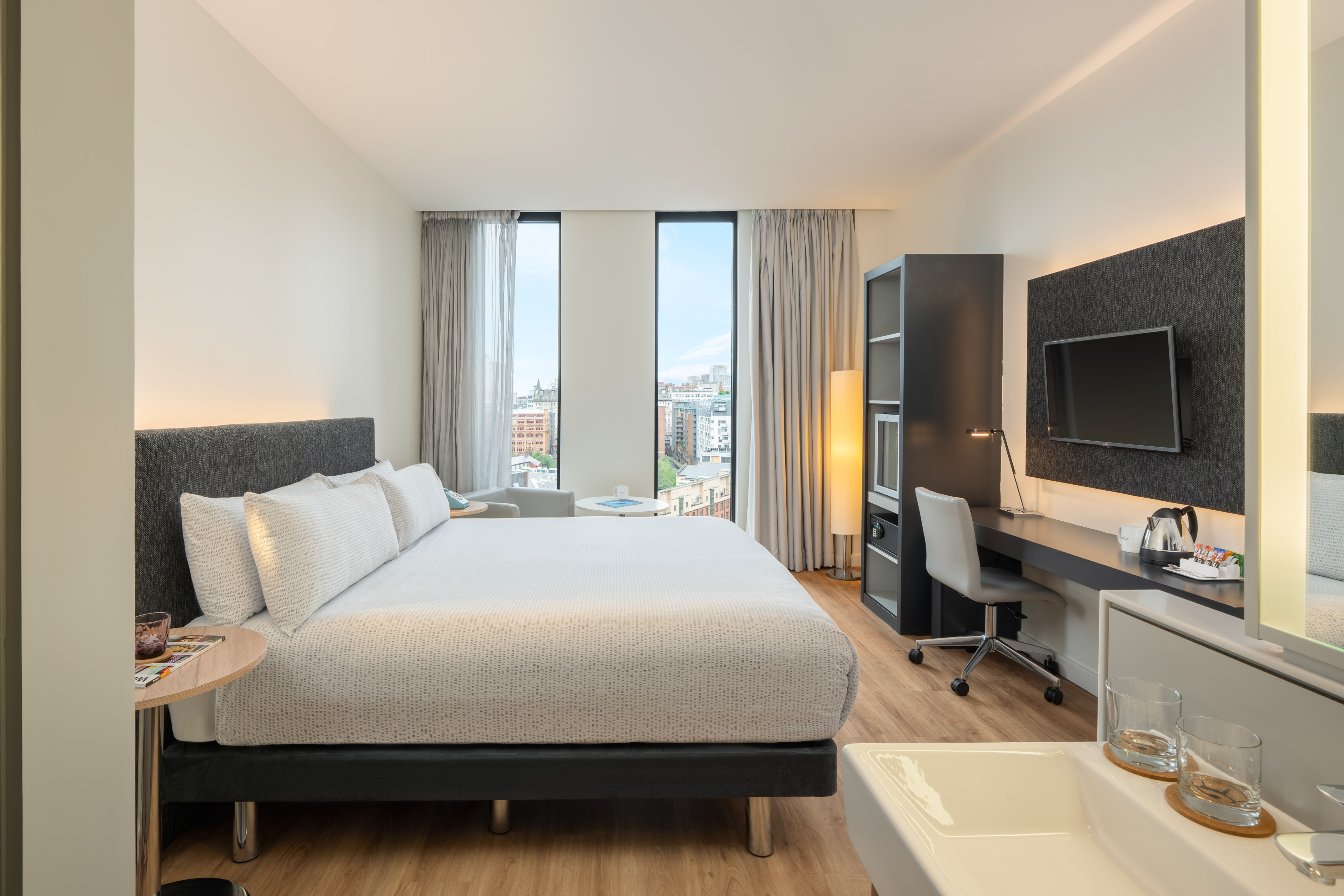 Contemporary hotel room with king bed, city view, and work desk.