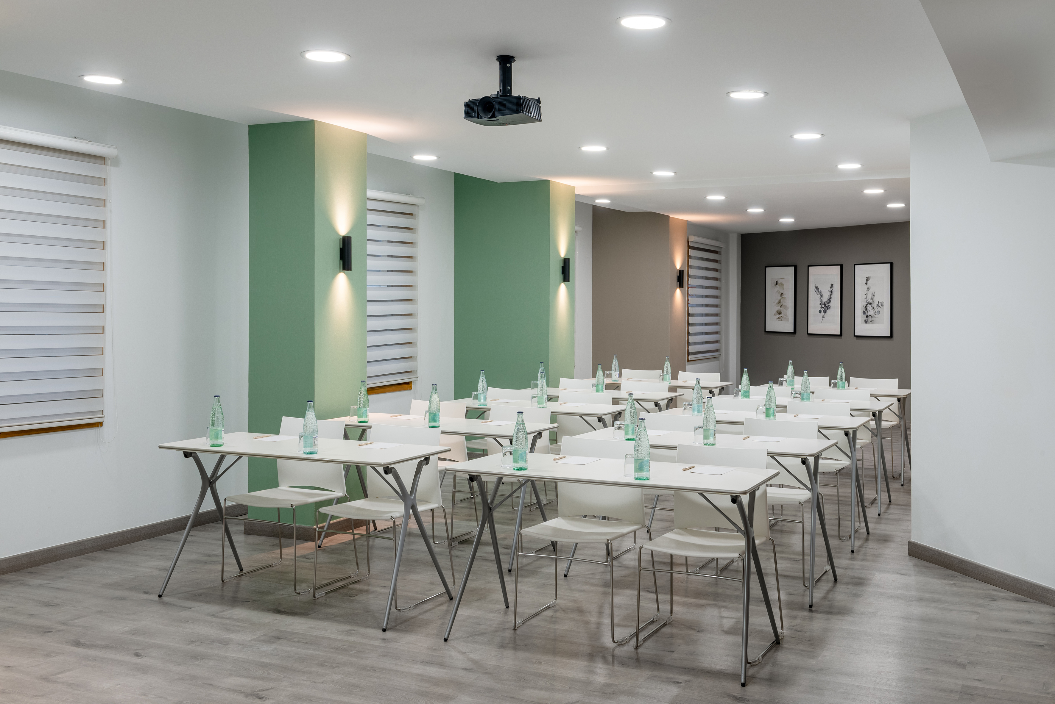 Modern meeting room with white tables, chairs, water bottles, and projector.