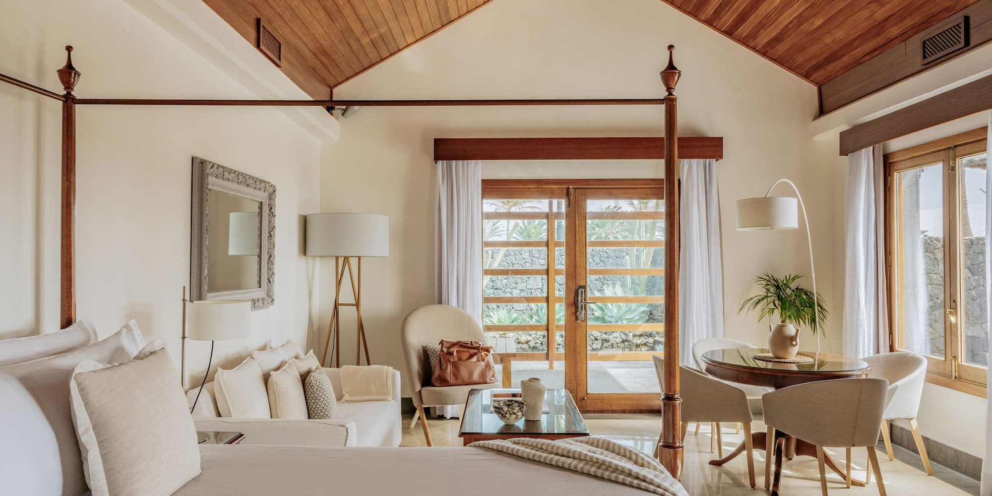 Luxury suite with four-poster bed, wooden ceiling, and tropical garden view.