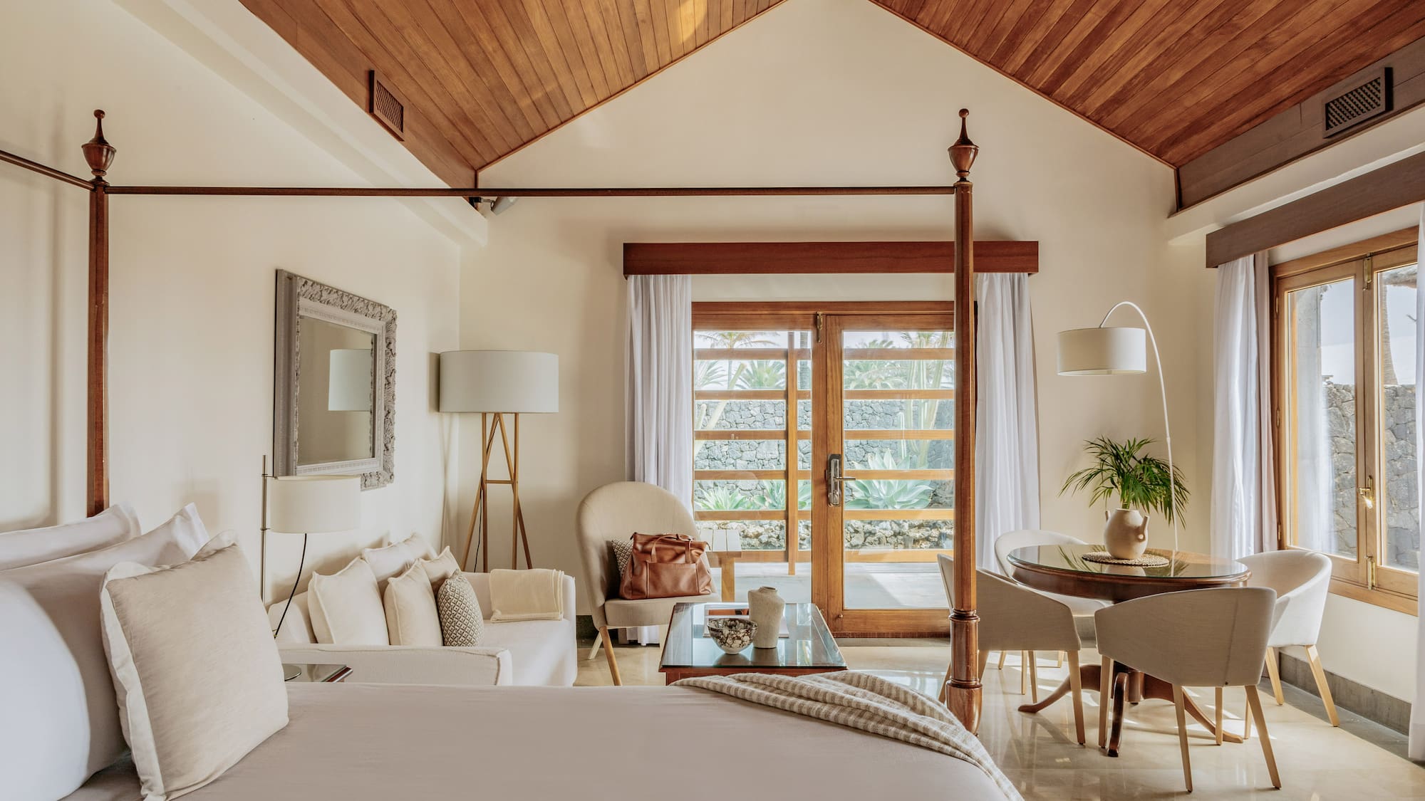 Luxury suite with four-poster bed, wooden ceiling, and tropical garden view.
