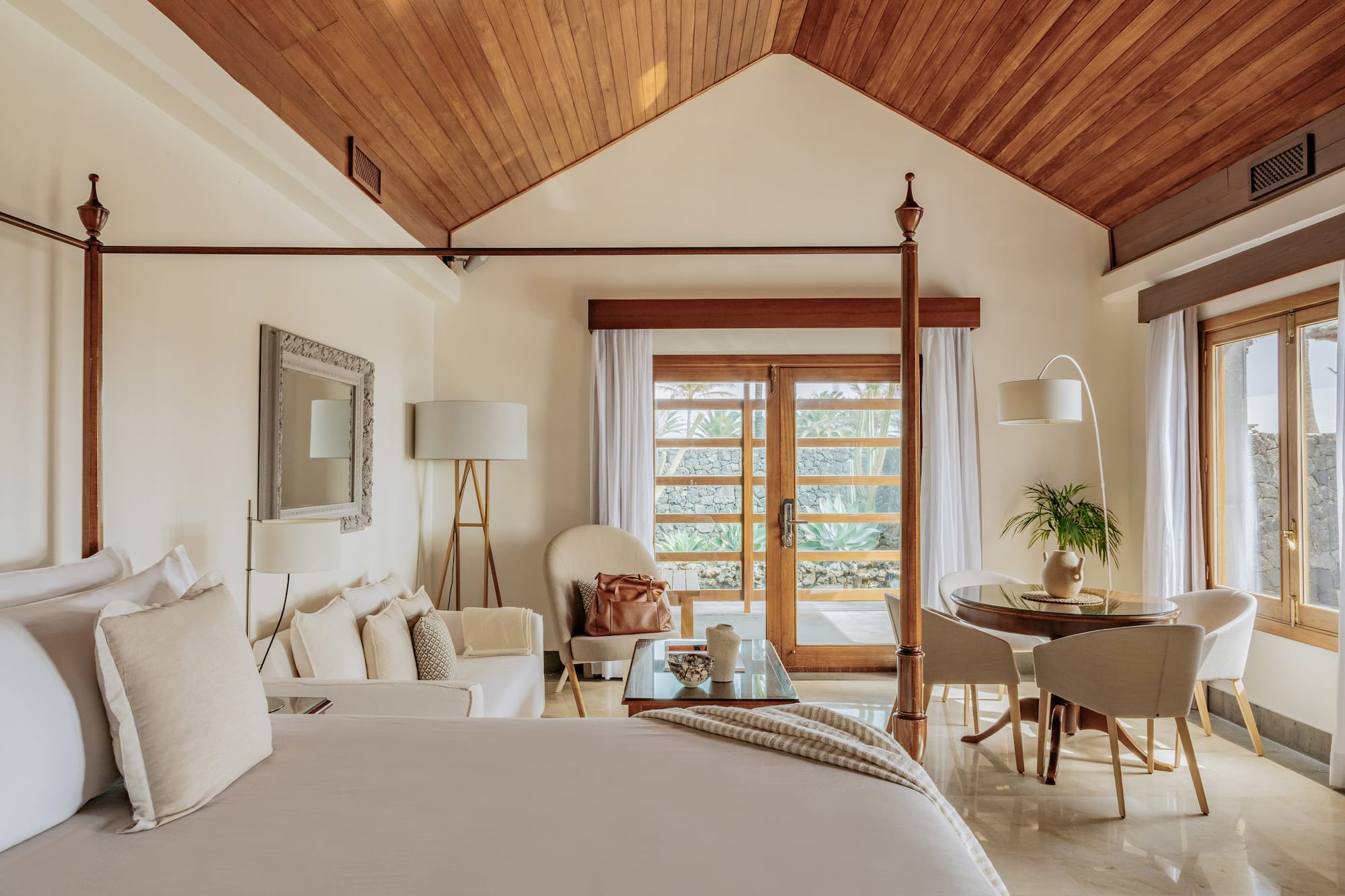 Luxury suite with four-poster bed, wooden ceiling, and tropical garden view.