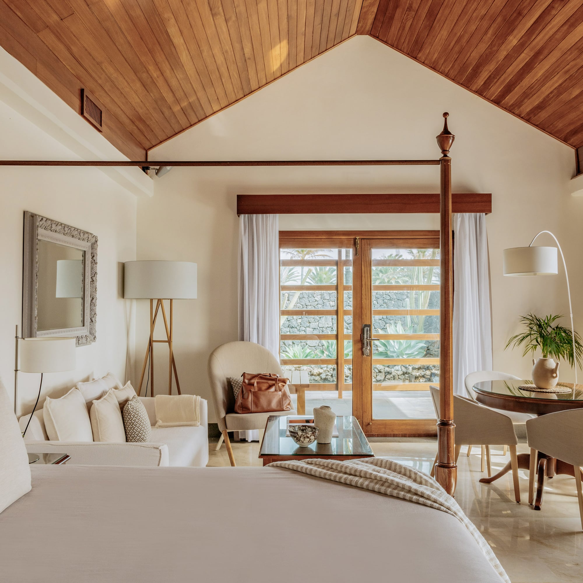 Luxury suite with four-poster bed, wooden ceiling, and tropical garden view.