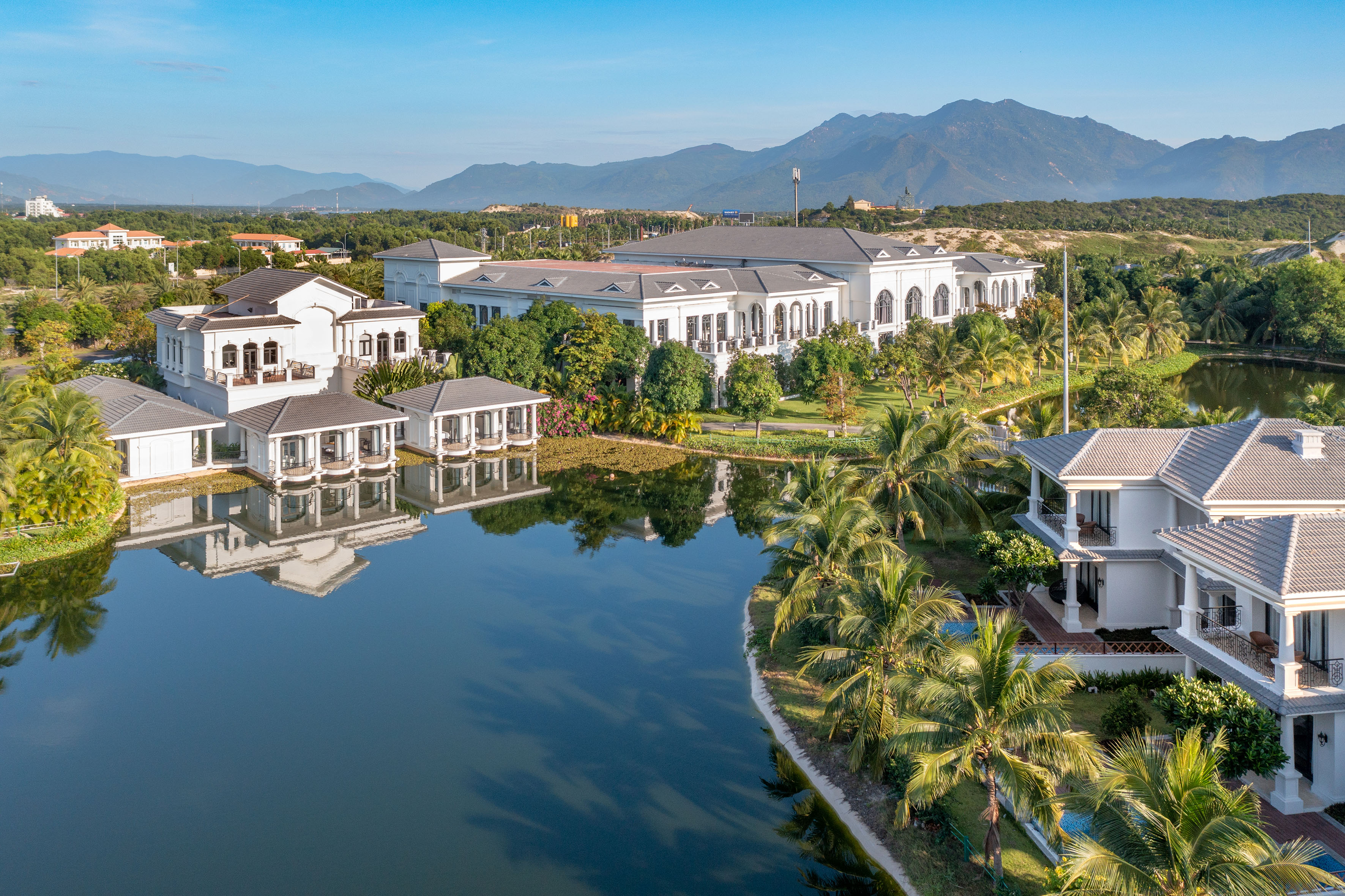 Lakeside luxury resort villas, palm trees, and distant mountains.