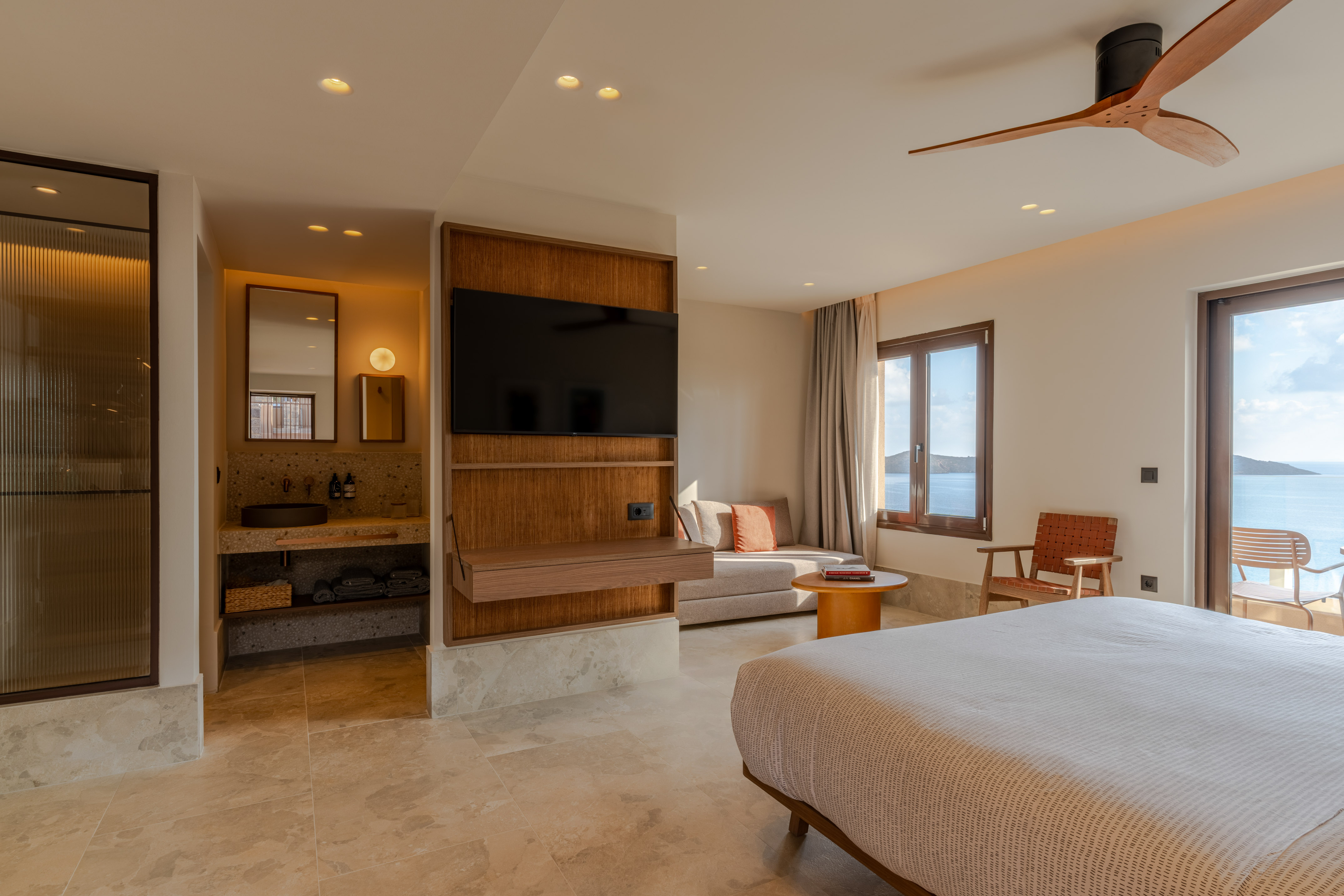 Luxury modern bedroom with ocean view, large bed, and wooden ceiling fan.