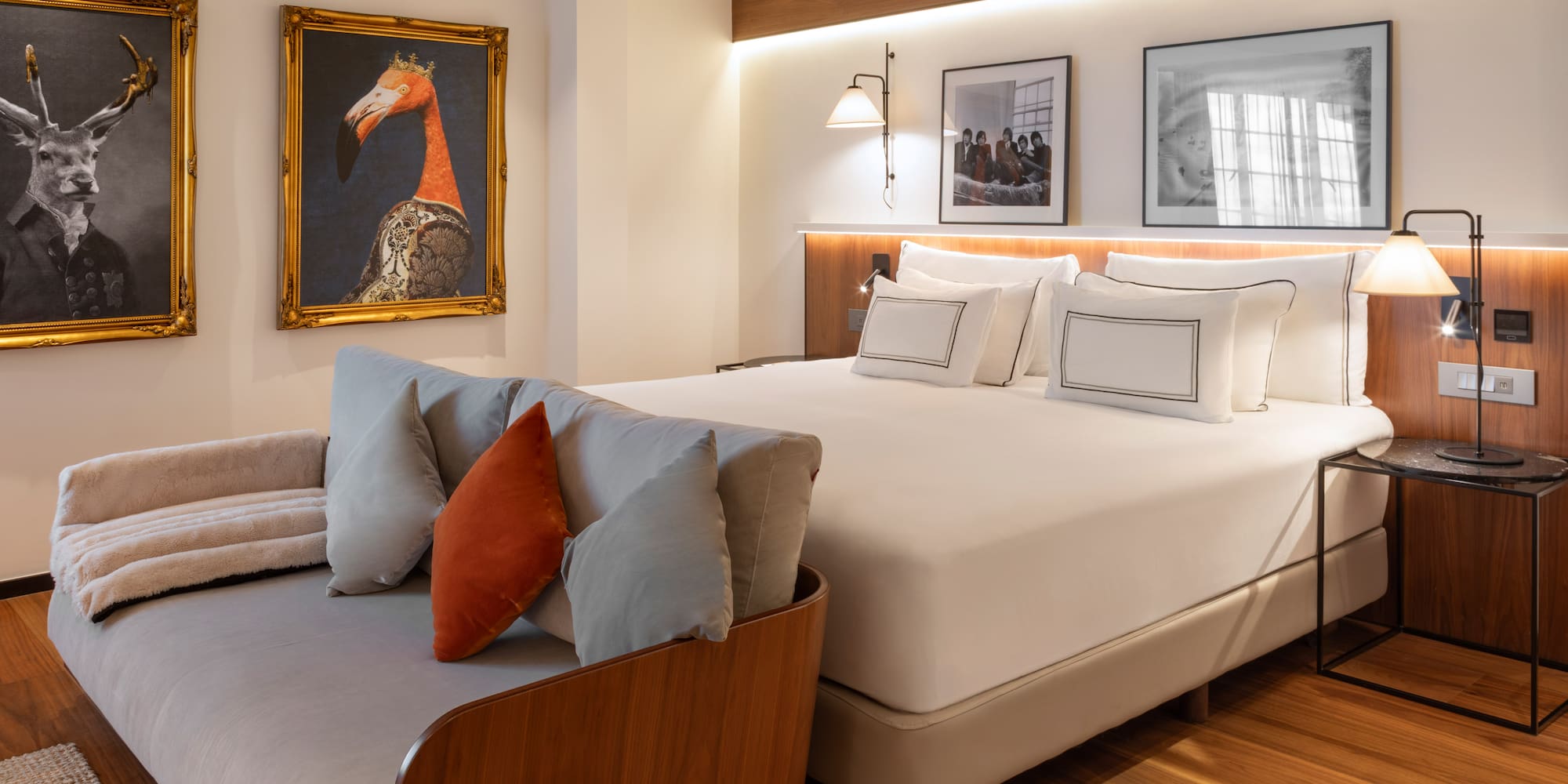 Modern hotel bedroom with large bed, gray sofa, and eclectic animal wall art.