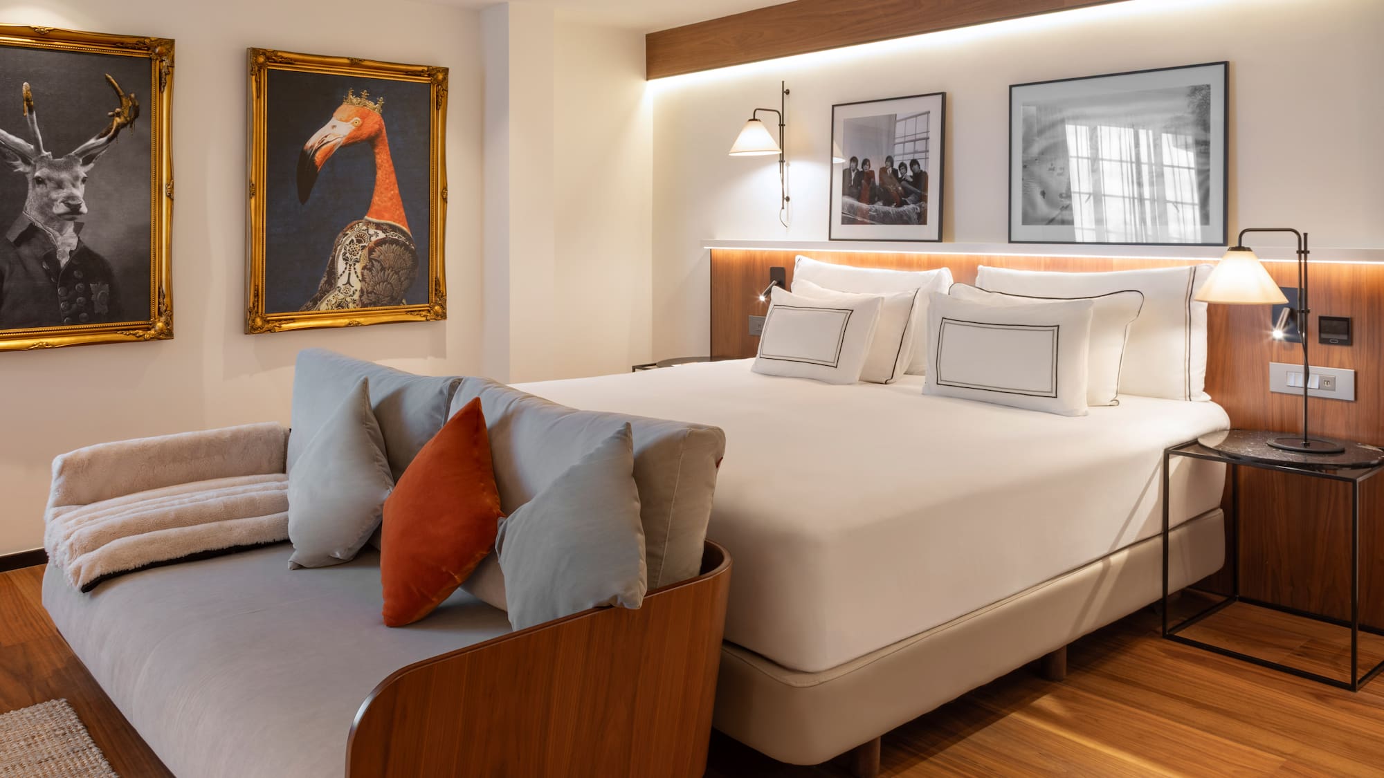 Modern hotel bedroom with large bed, gray sofa, and eclectic animal wall art.