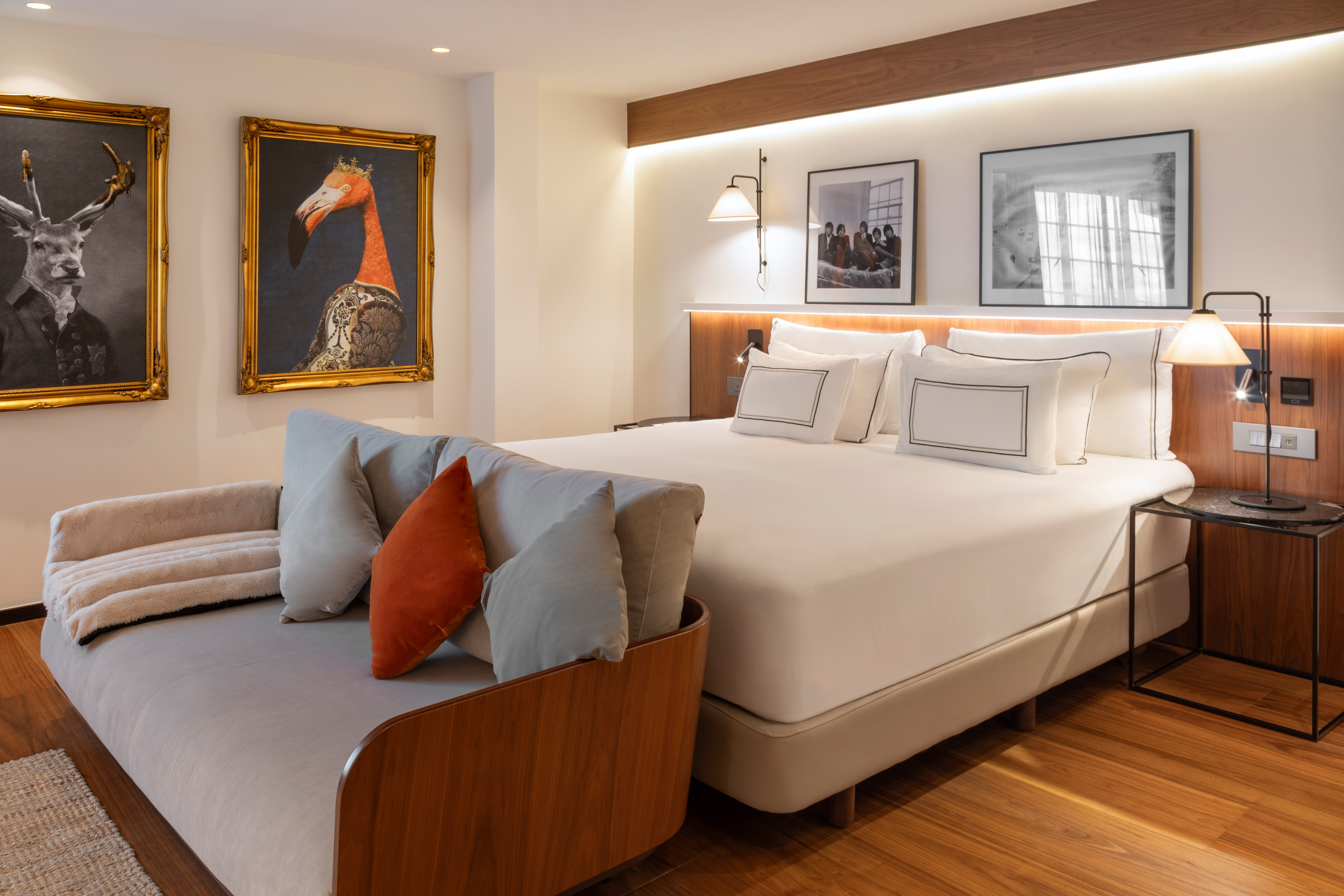 Modern hotel bedroom with large bed, gray sofa, and eclectic animal wall art.