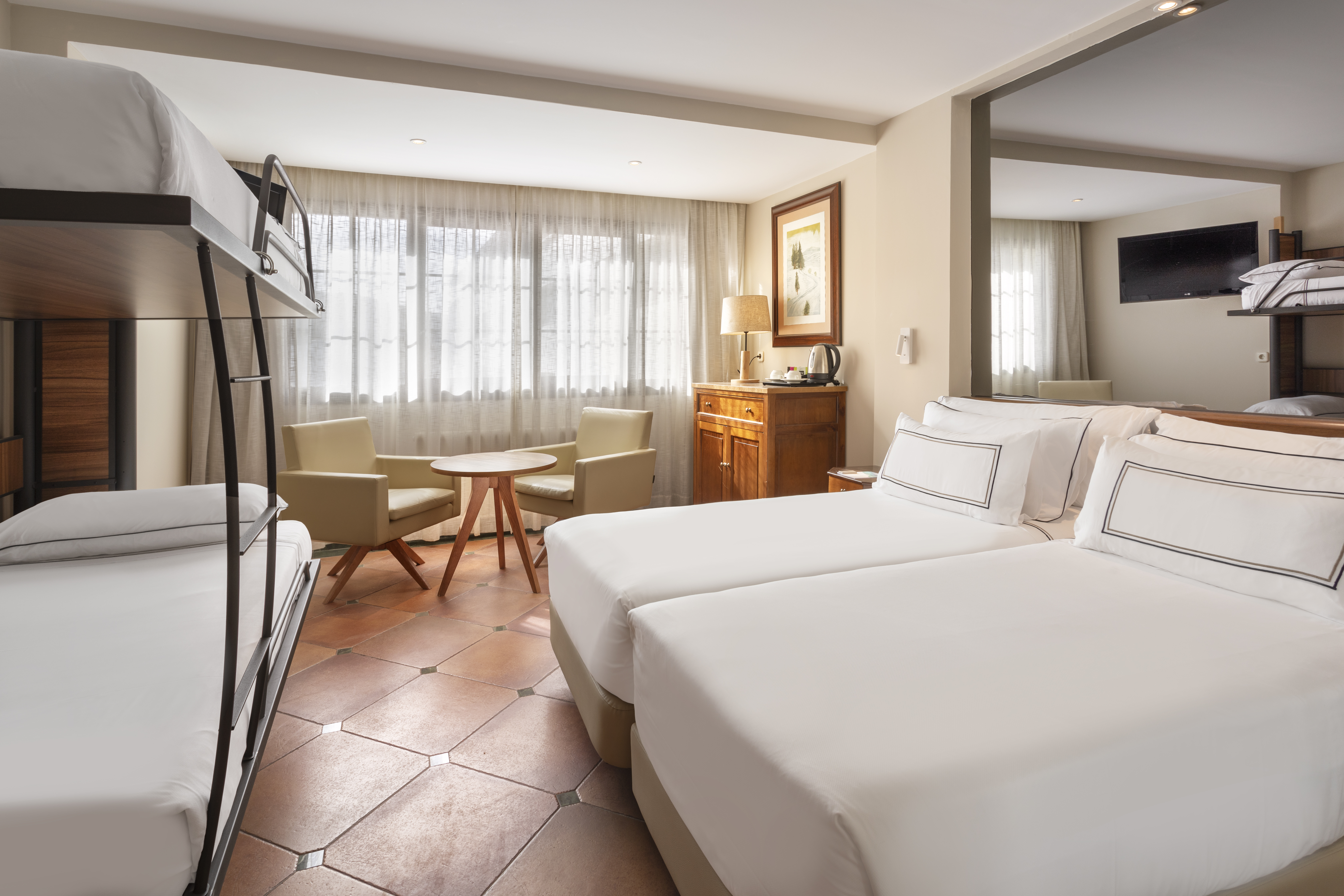 Hotel family room with bunk bed, twin beds, sitting area, terracotta tiled floor.
