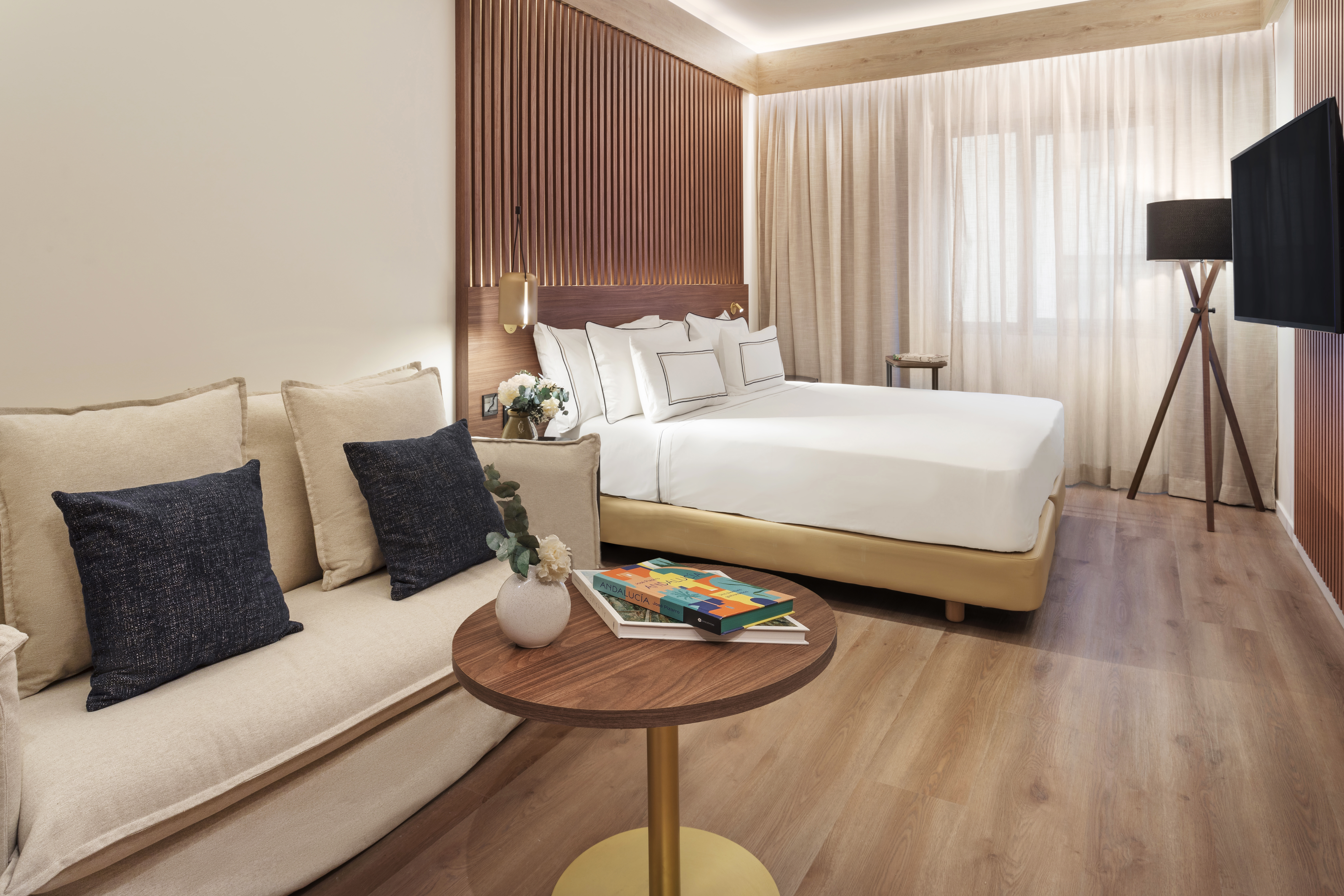 Stylish hotel room: bed, sofa, wooden headboard, modern decor, and soft lighting.