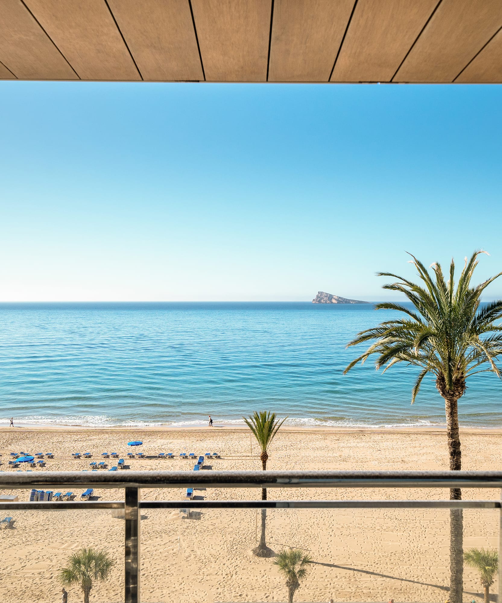 Benidorm beach from hotel balcony: sunny sea, sand, palm trees, distant island.