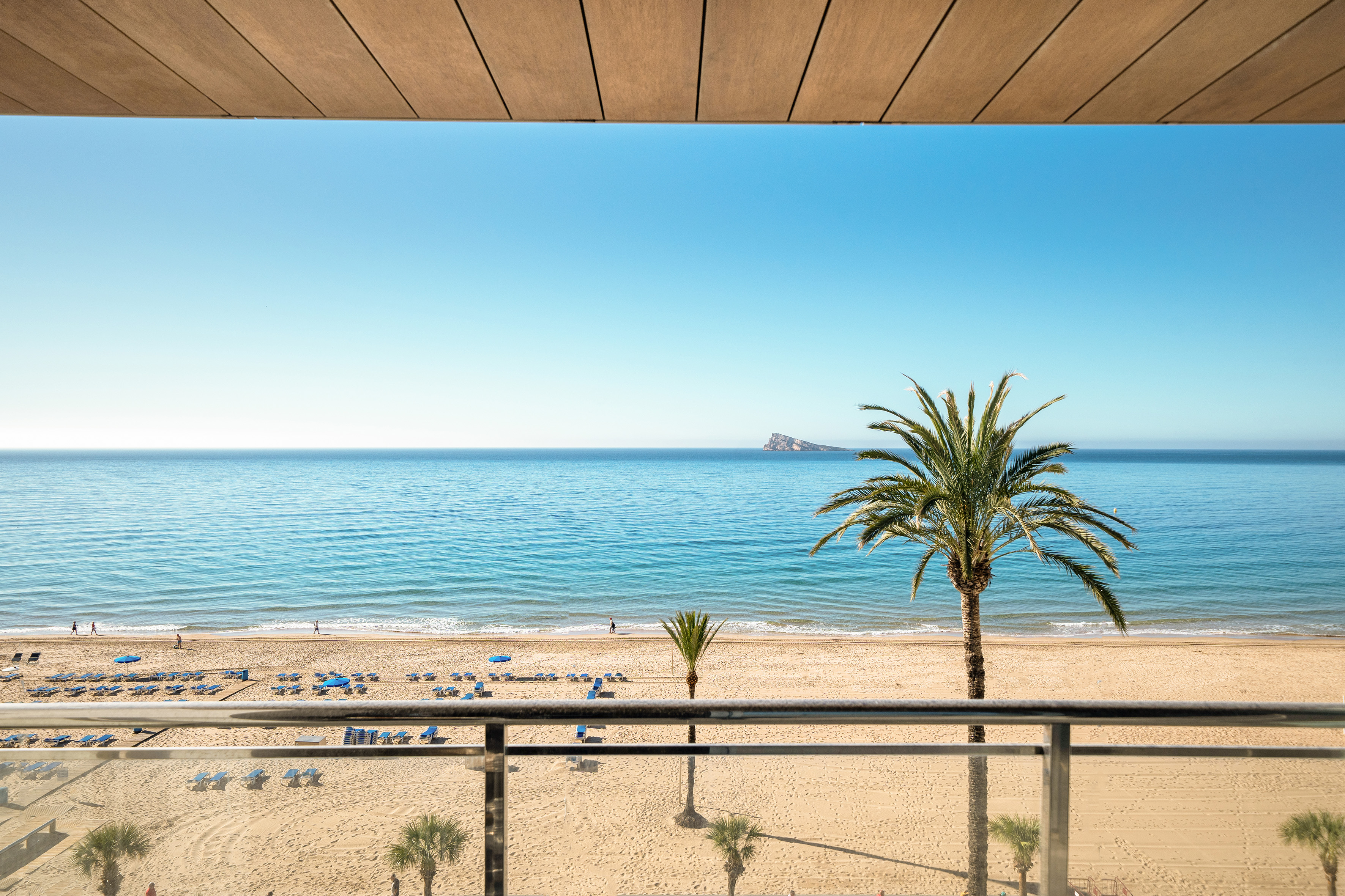 Benidorm beach from hotel balcony: sunny sea, sand, palm trees, distant island.