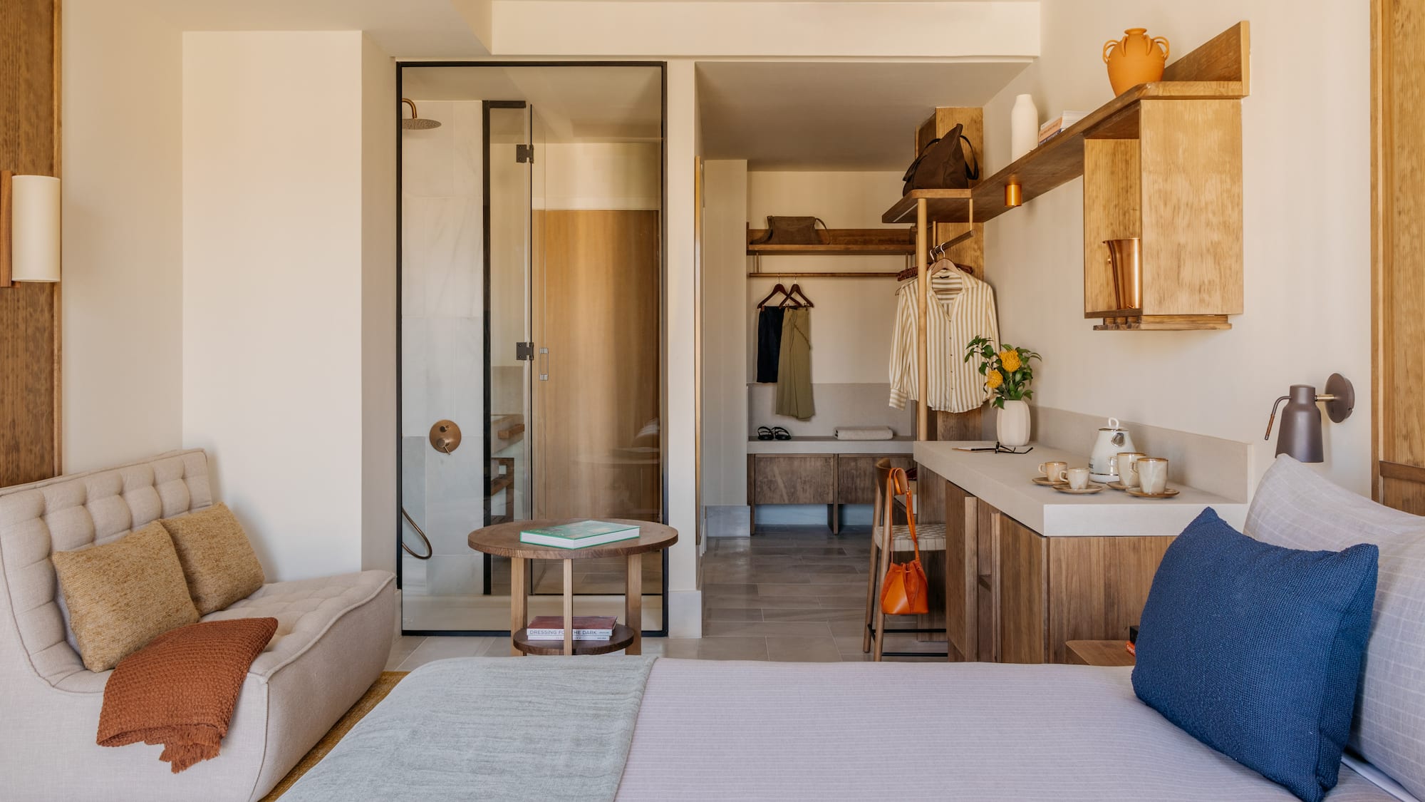 Modern hotel room with bed, glass shower, open closet, and wood details.
