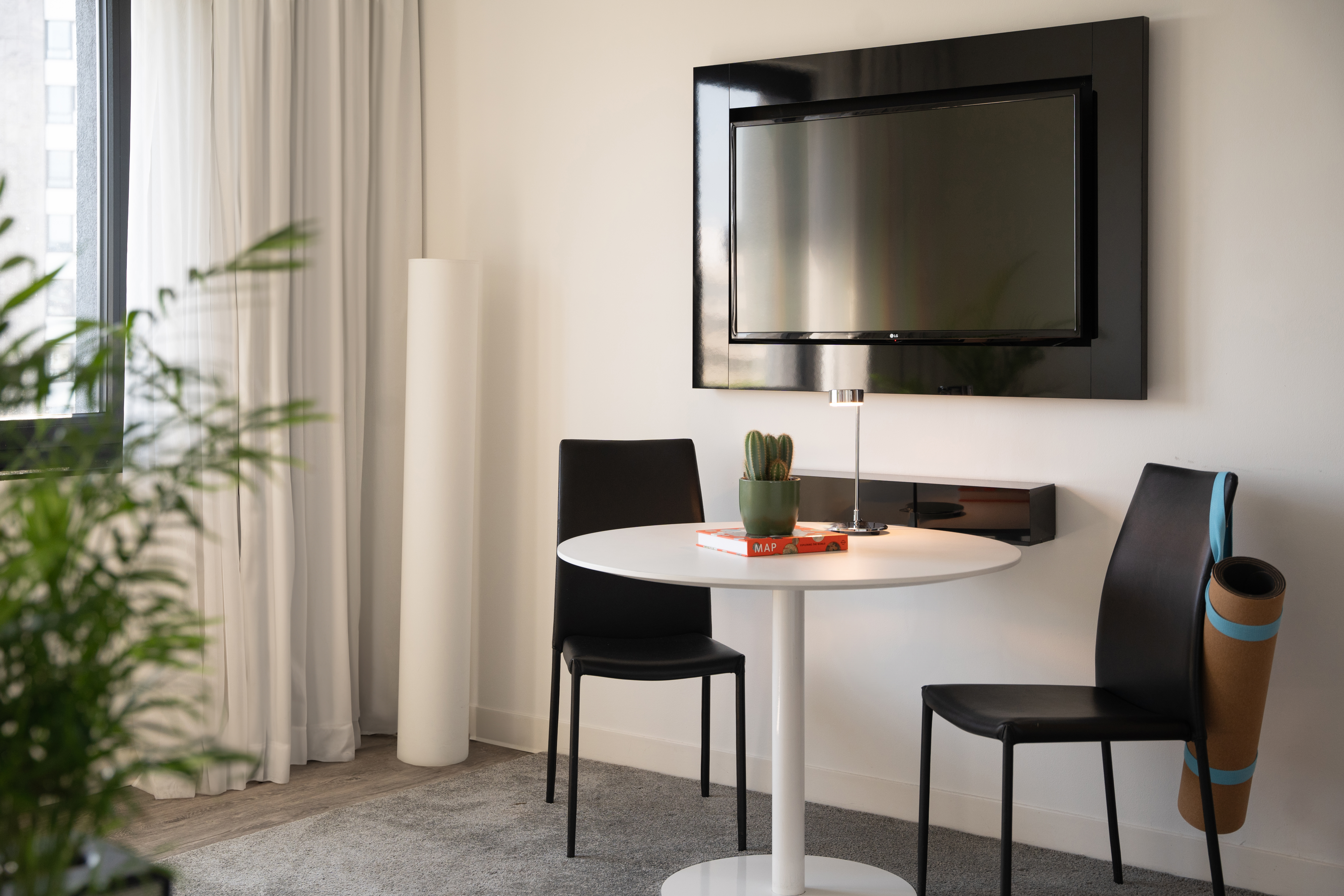 Modern room with TV, white table, black chairs, cactus, and yoga mat.