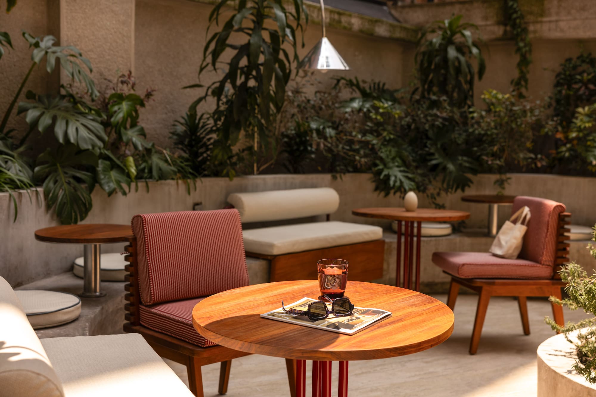 Modern outdoor patio with wooden tables, striped chairs, and lush plants.