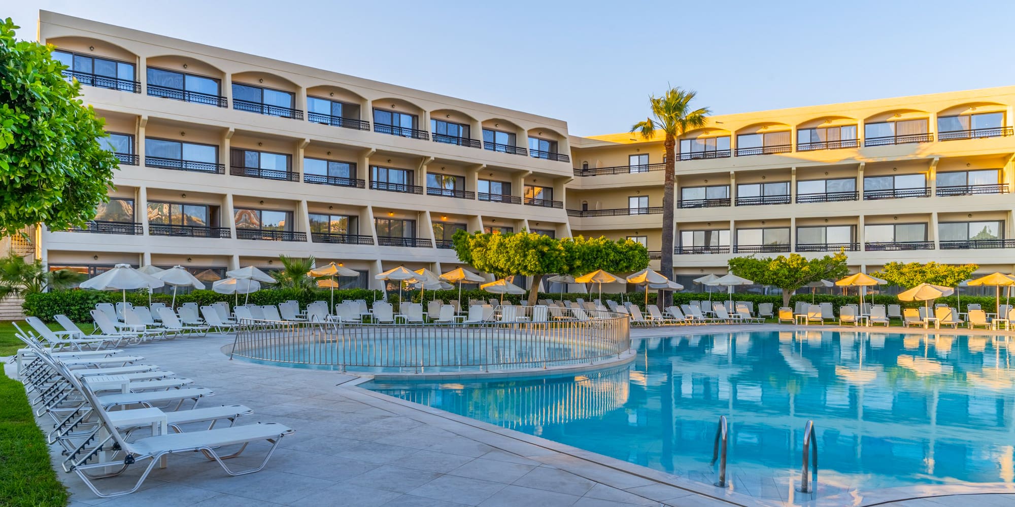 Hotel resort with outdoor swimming pool, many lounge chairs, and palm trees.