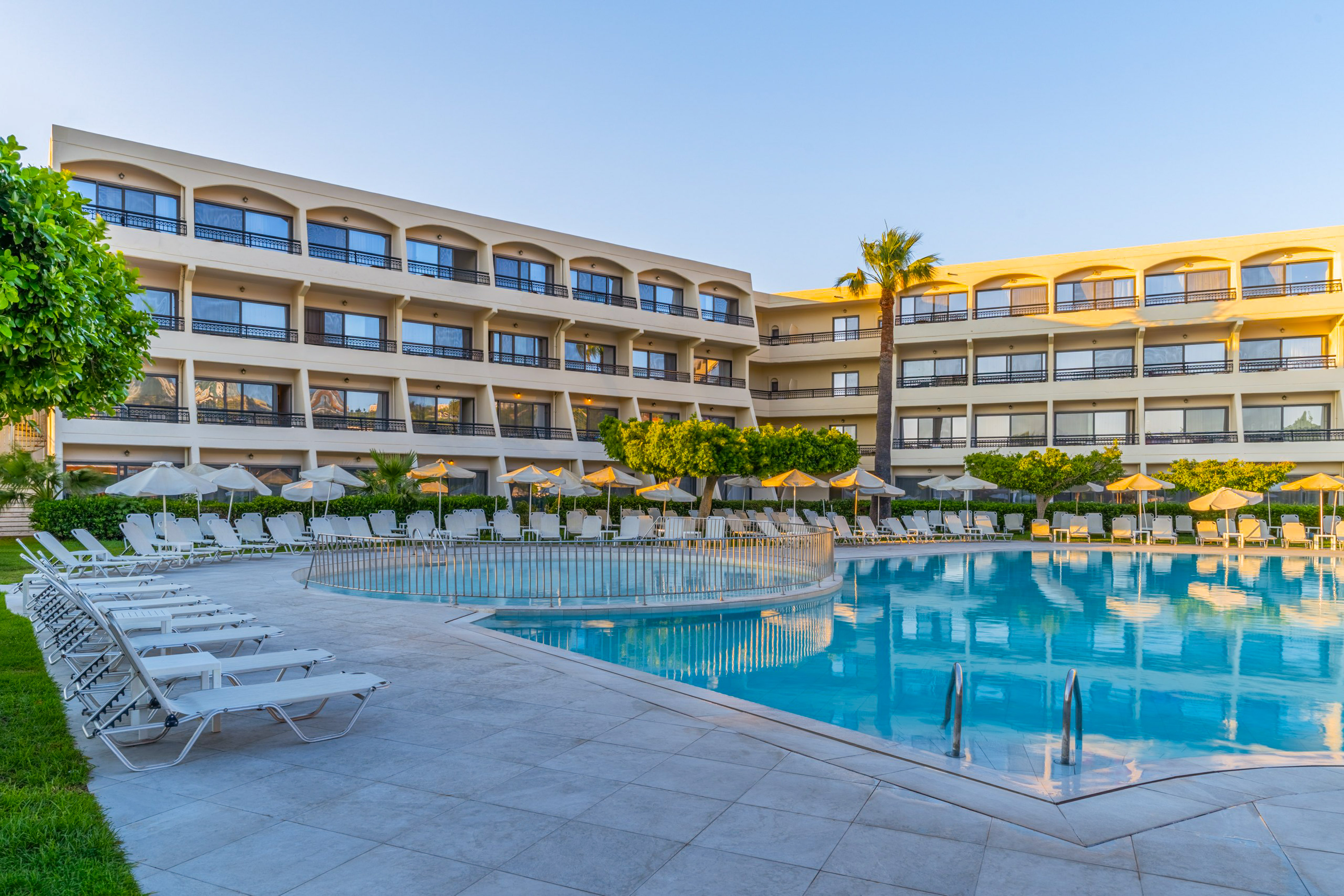 Hotel resort with outdoor swimming pool, many lounge chairs, and palm trees.