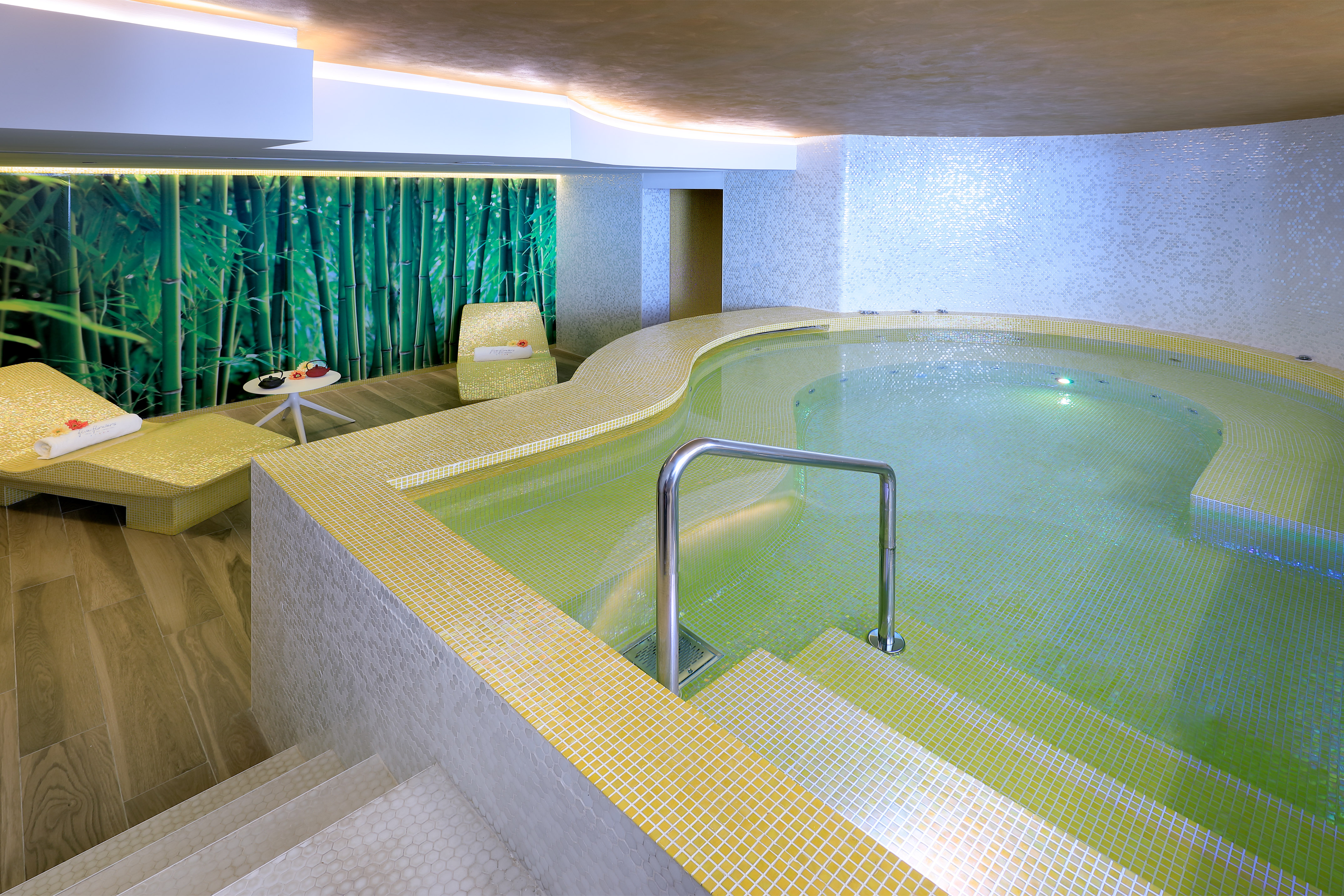 Spa jacuzzi with yellow mosaic tiles, bamboo wall mural, and lounge chairs.