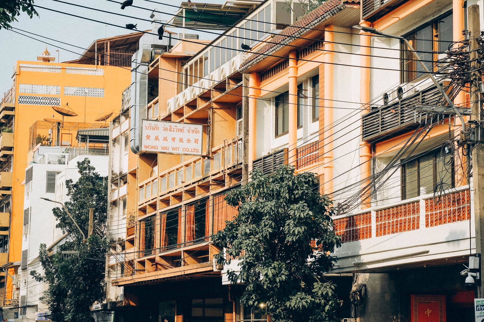 Bangkok street view: orange buildings, tangled wires, 'WONG WAI WIT' sign.