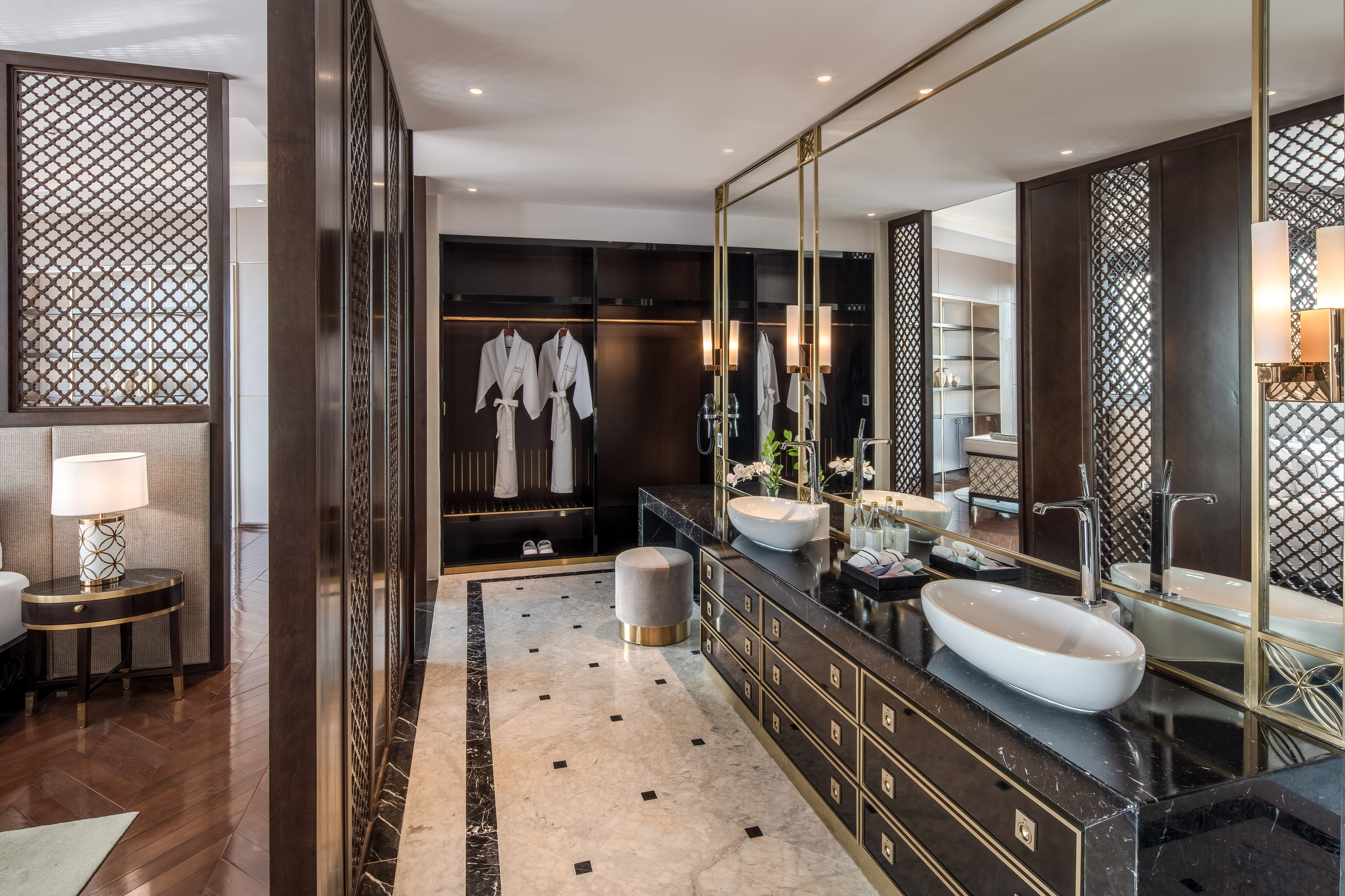 Luxury bathroom with double vanity, marble, dark wood closet, and bathrobes.