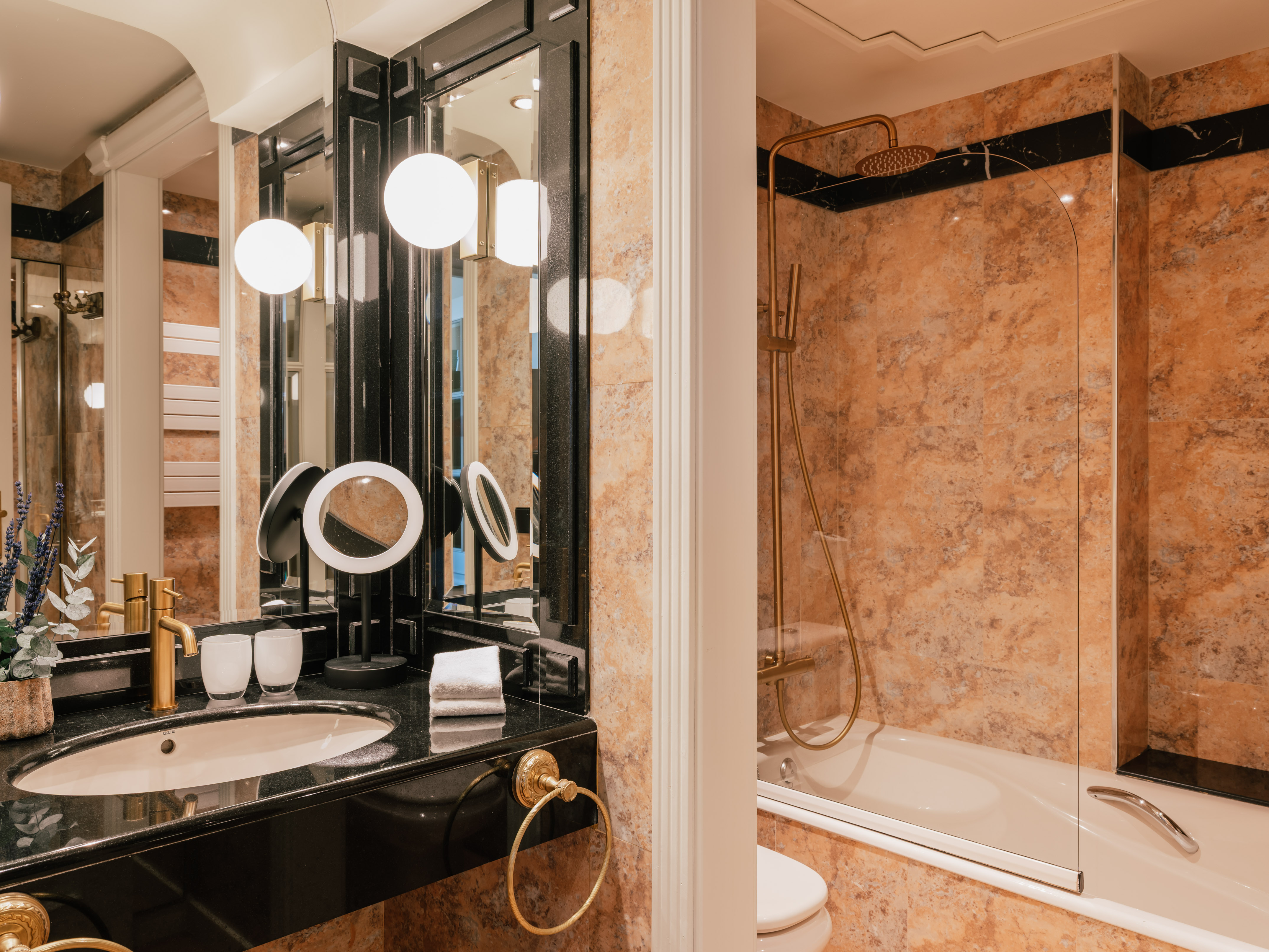 Elegant bathroom with black marble vanity, gold fixtures, and marble-tiled shower/tub.