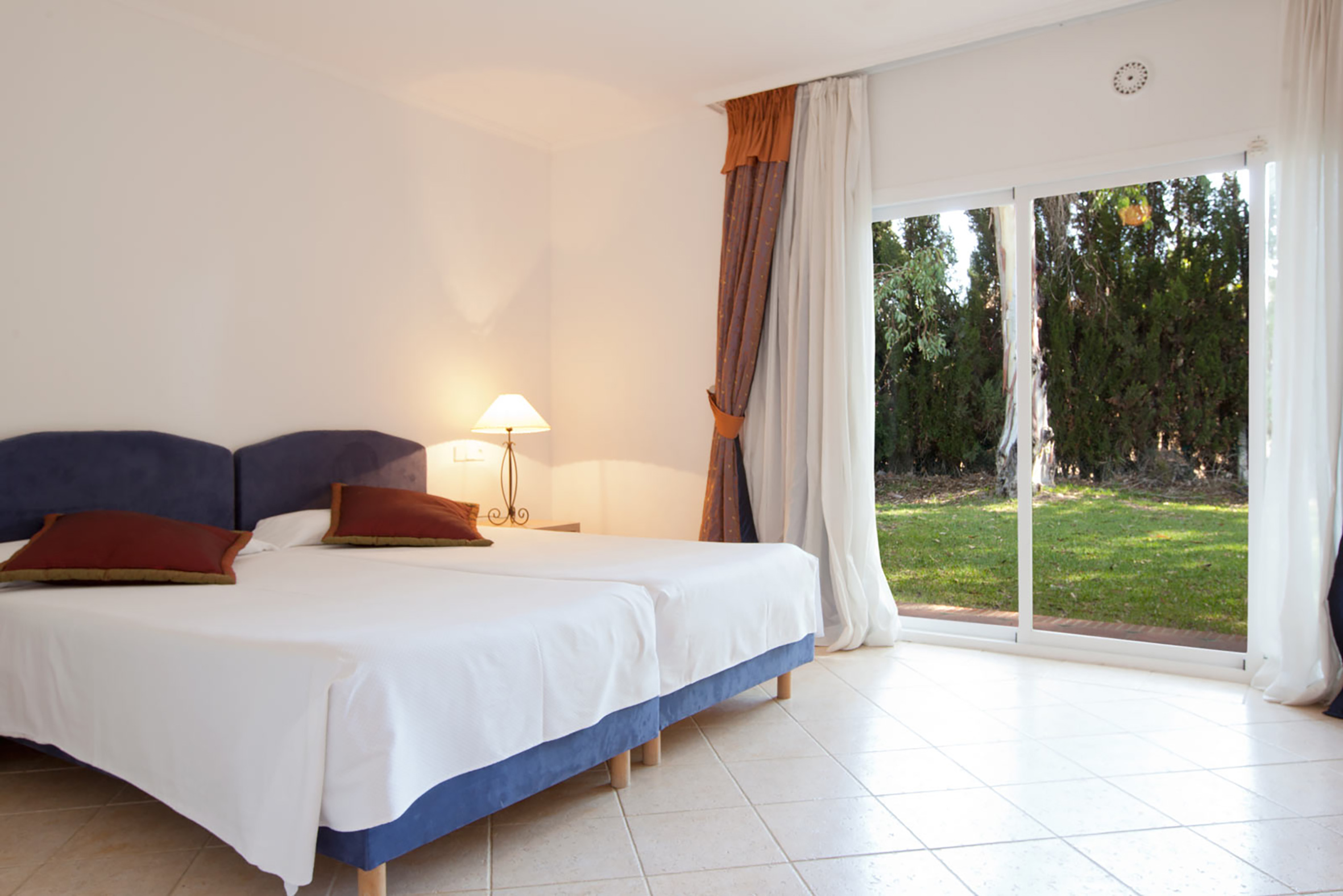 Hotel bedroom with twin beds, lamp, and sliding patio door to garden.