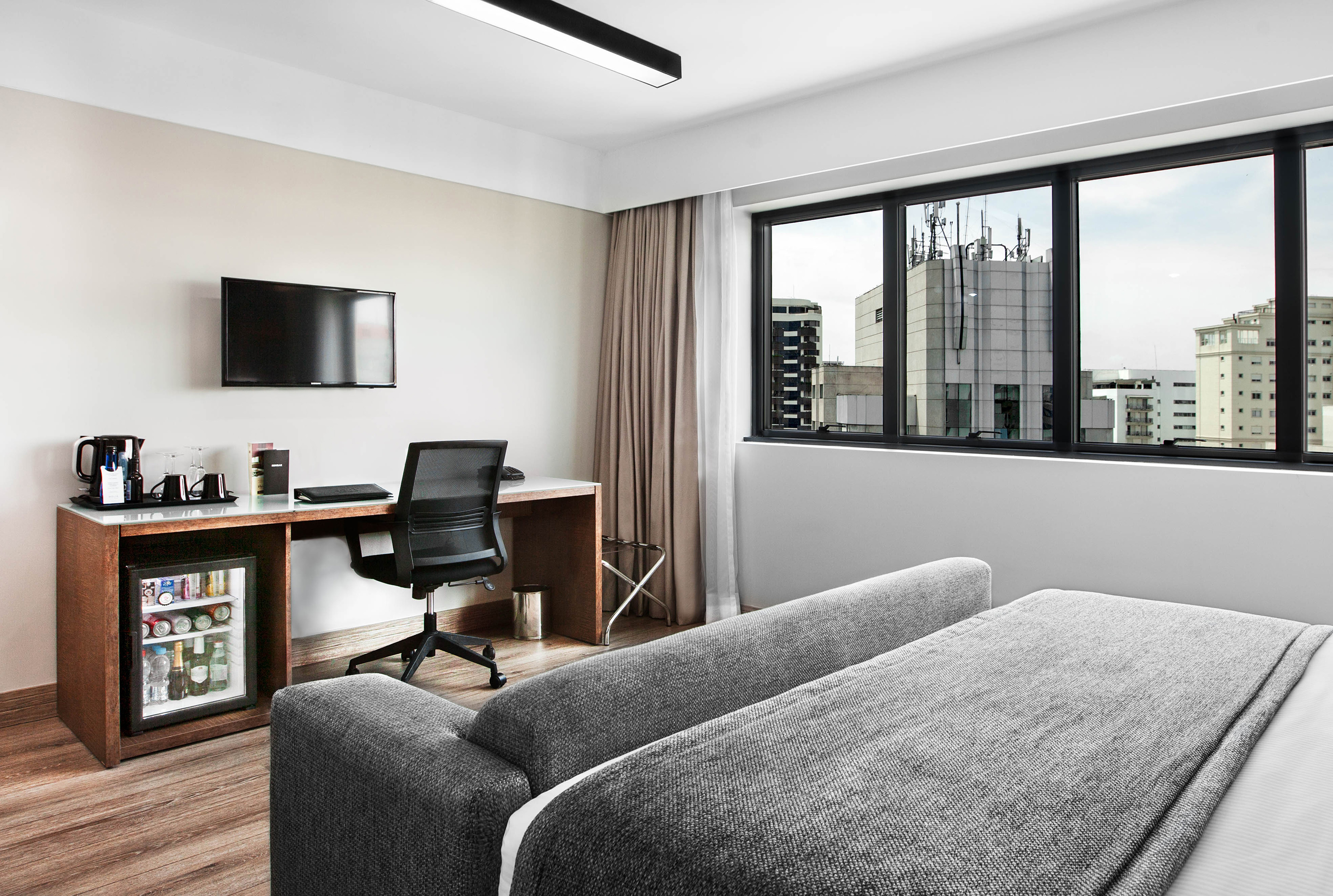 Modern hotel room with desk, TV, minibar, and city view.