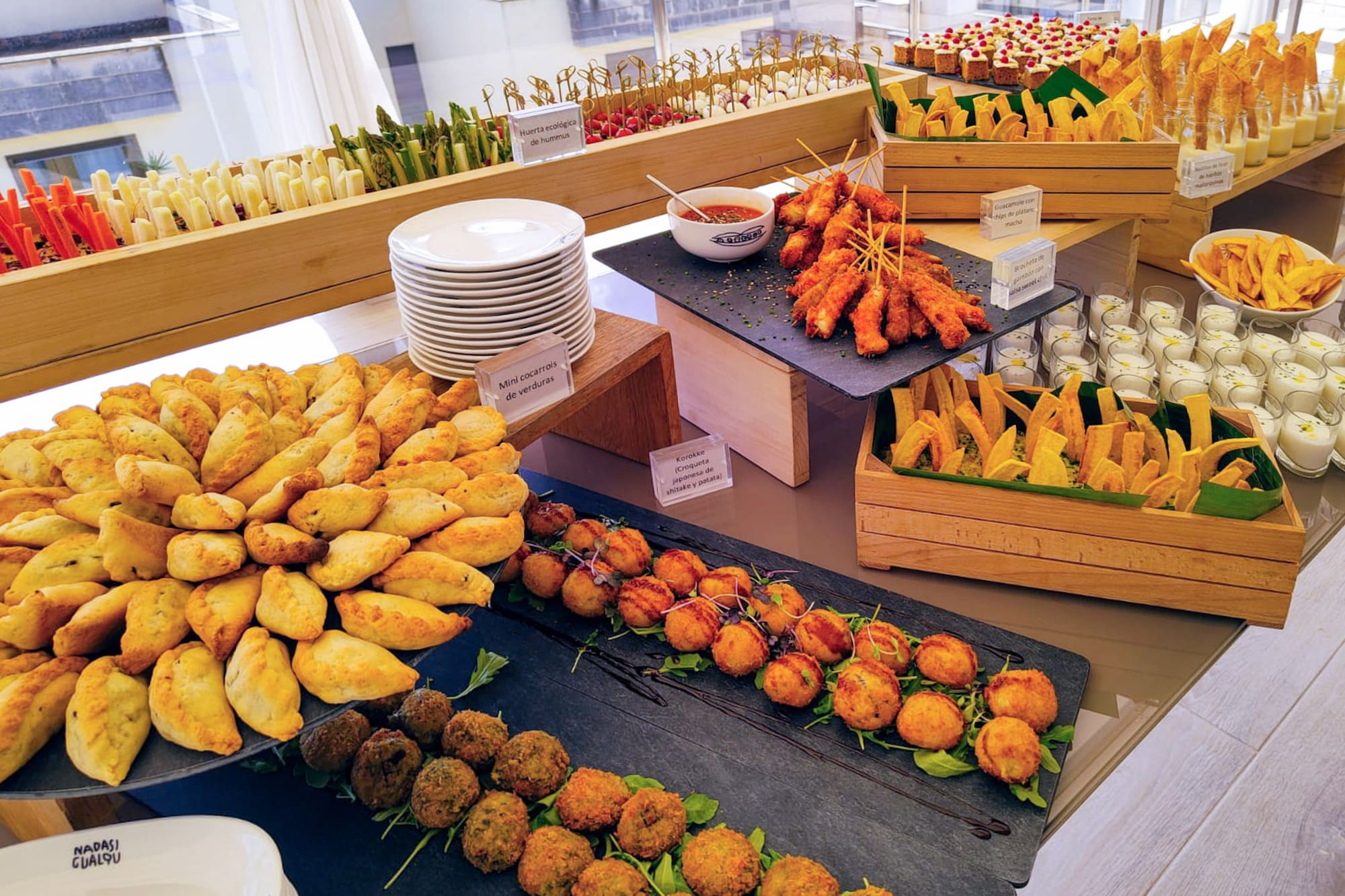 Gourmet buffet spread with empanadas, croquettes, skewers, and fresh vegetables.