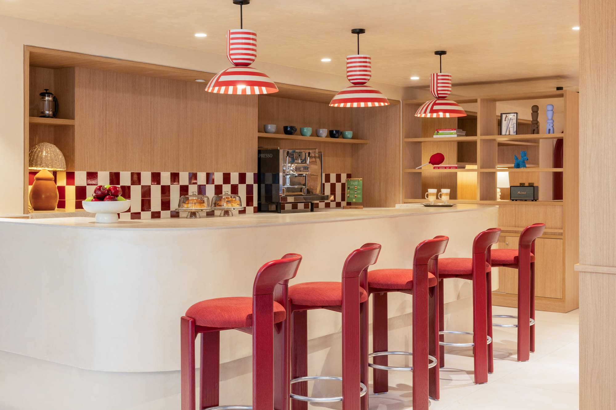 Modern bar with red stools, striped lights, and checkered backsplash.