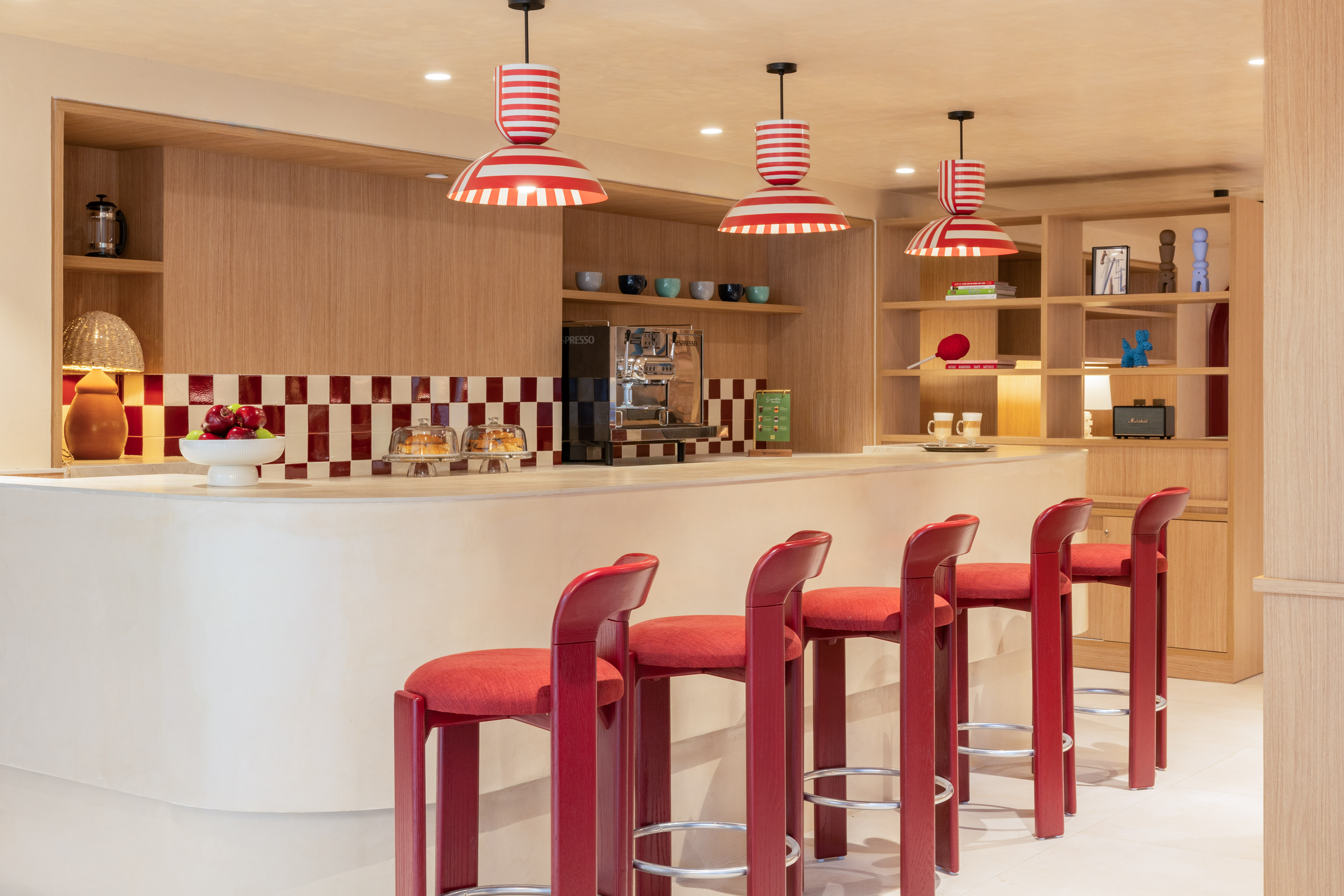 Modern bar with red stools, striped lights, and checkered backsplash.