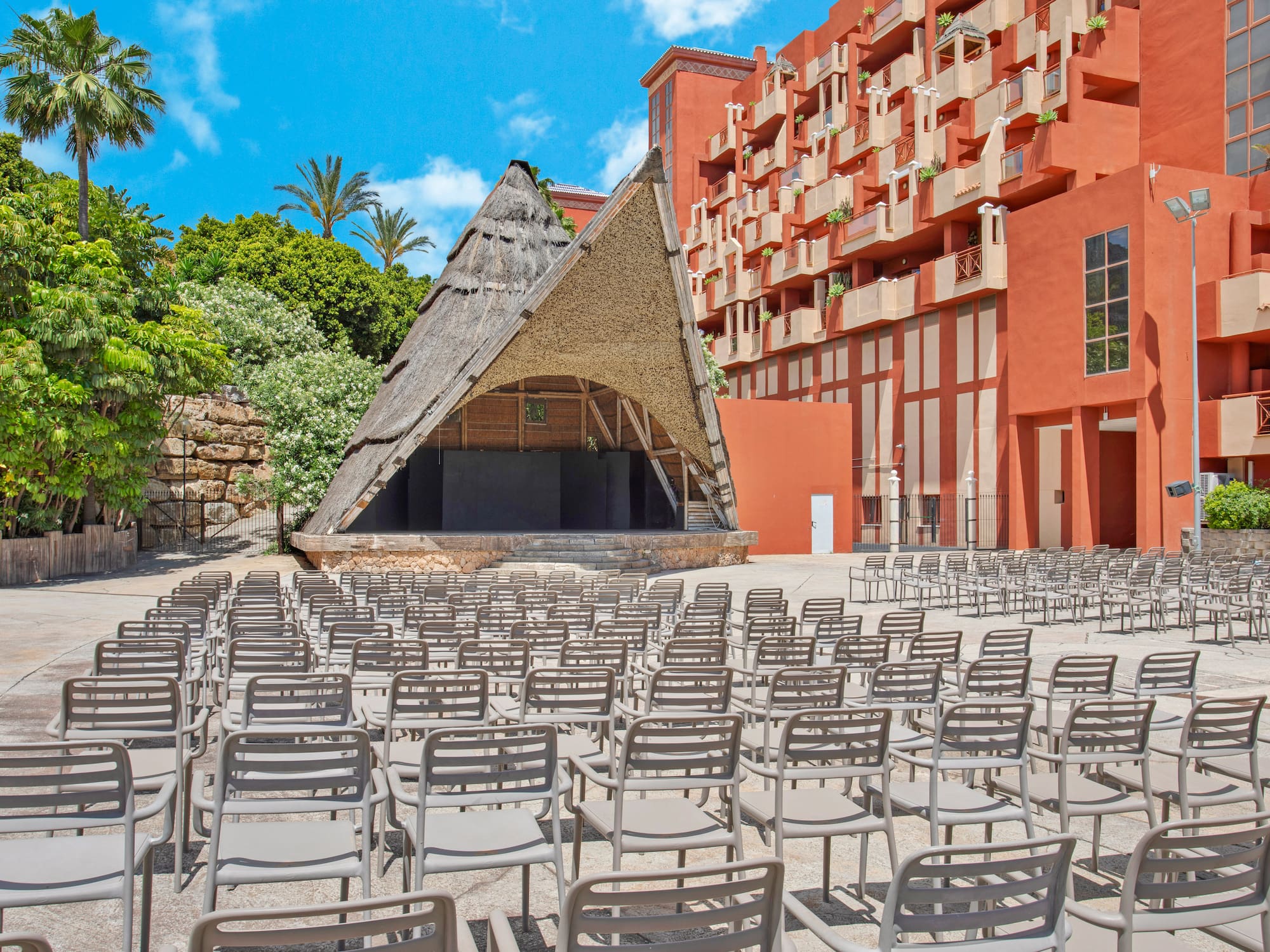 Tropical resort outdoor event space with thatched stage, empty seating.