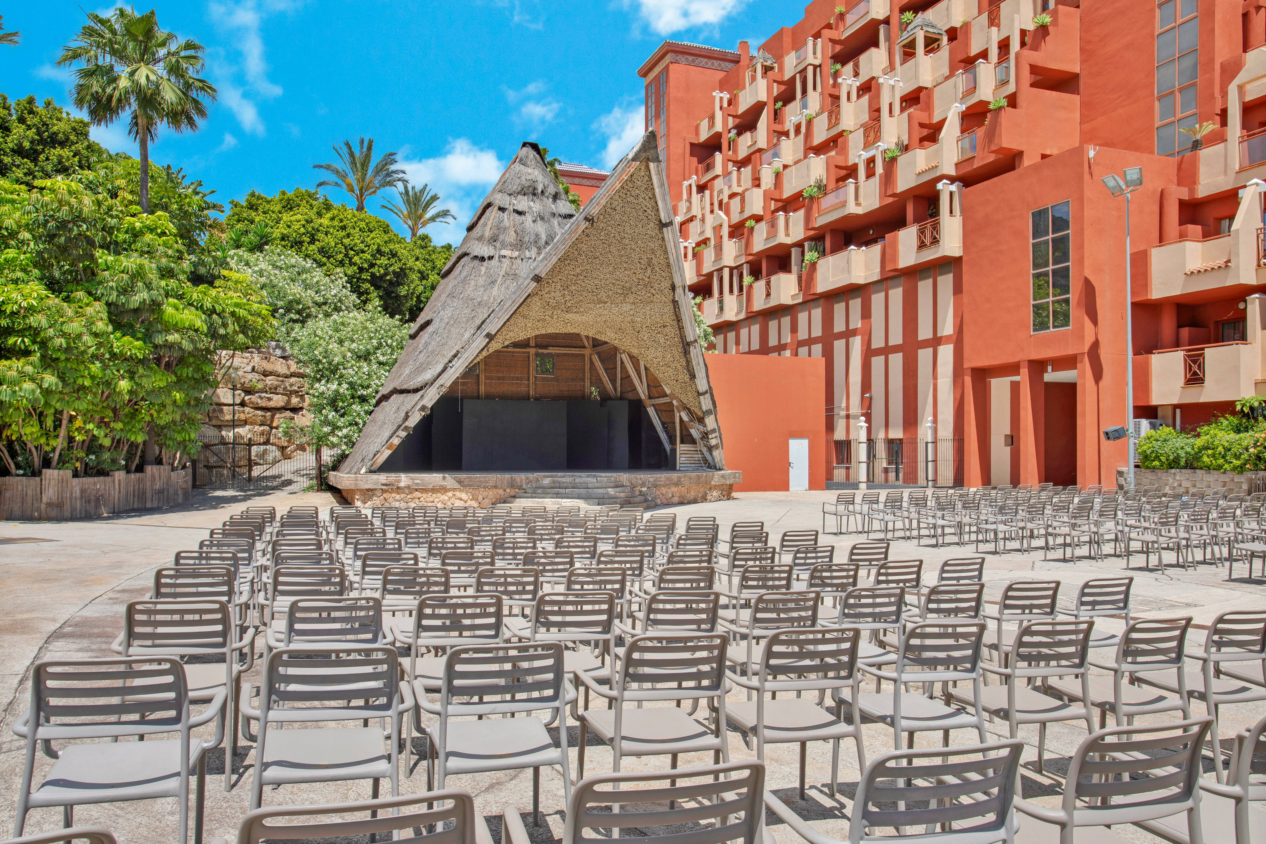 Tropical resort outdoor event space with thatched stage, empty seating.