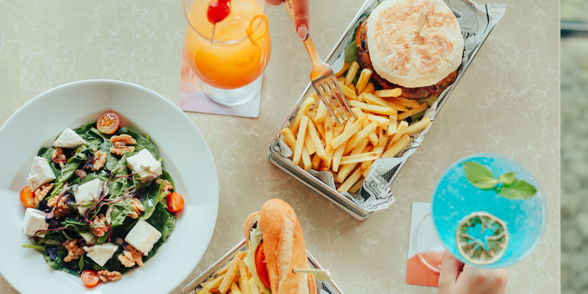 Restaurant meal: burger, fries, salad, sandwich, and vibrant cocktails.