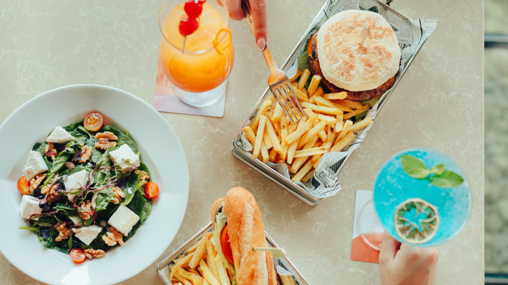Restaurant meal: burger, fries, salad, sandwich, and vibrant cocktails.