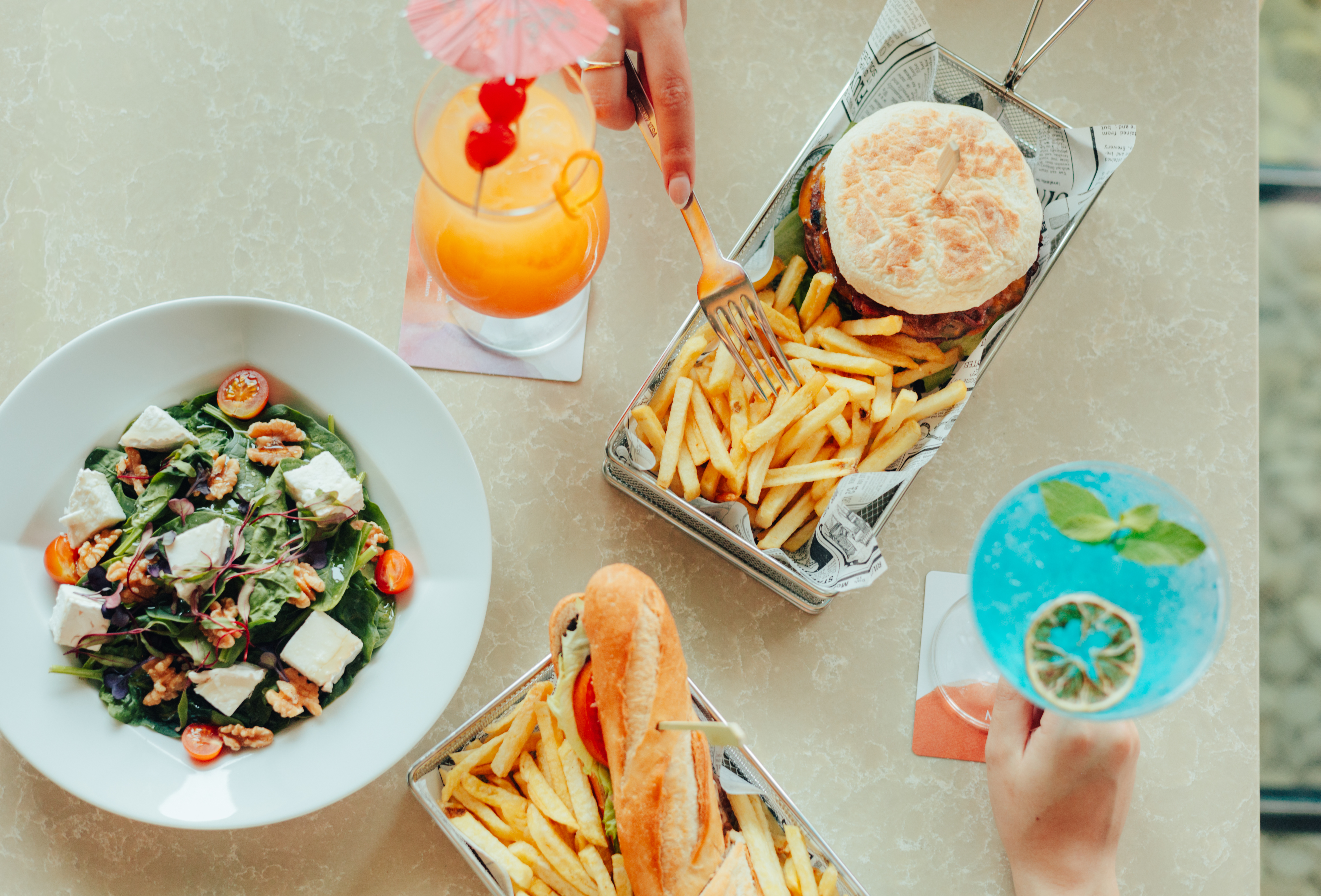Restaurant meal: burger, fries, salad, sandwich, and vibrant cocktails.