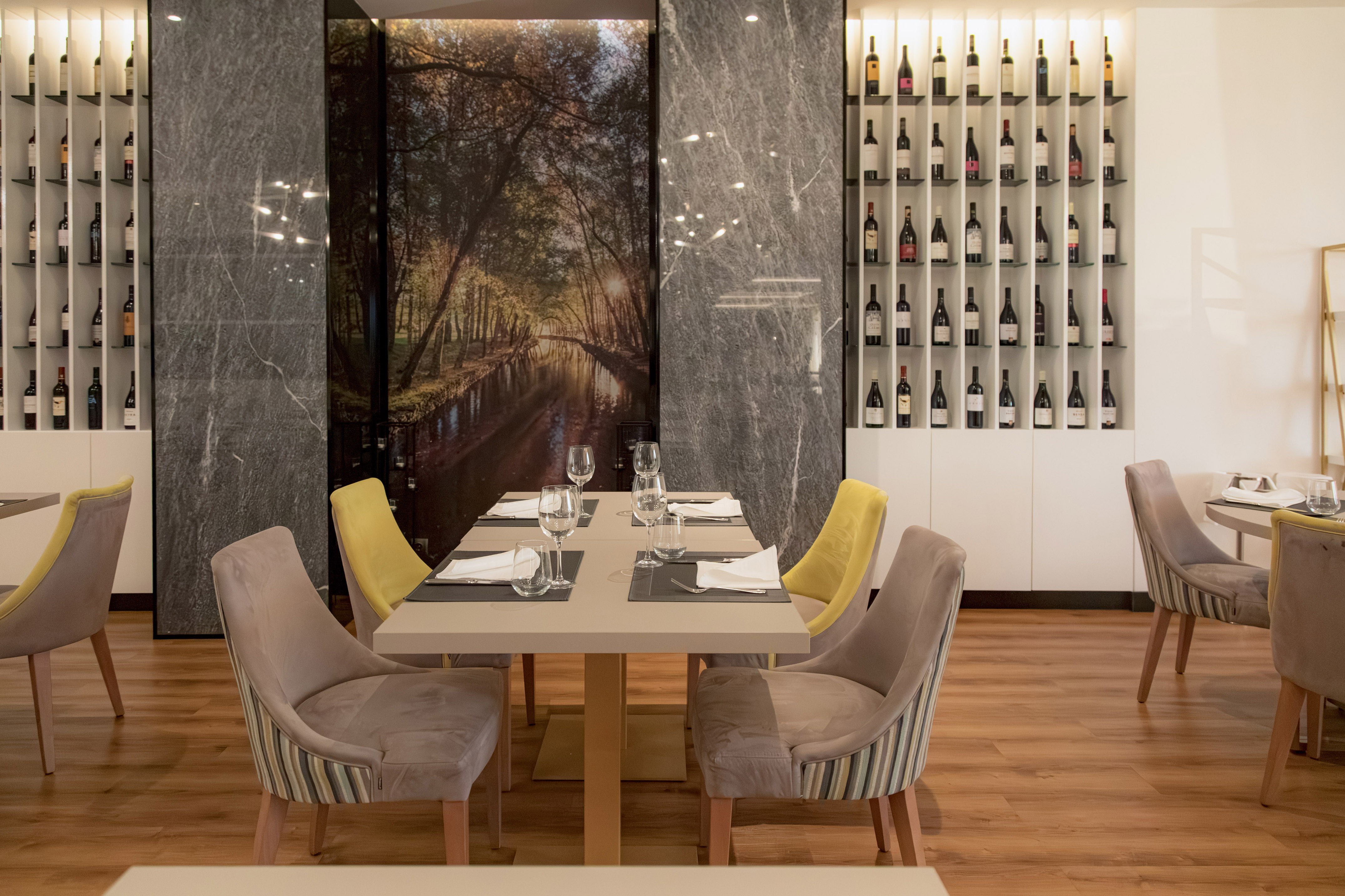 Modern restaurant interior with wine walls, elegant table settings, and forest mural.