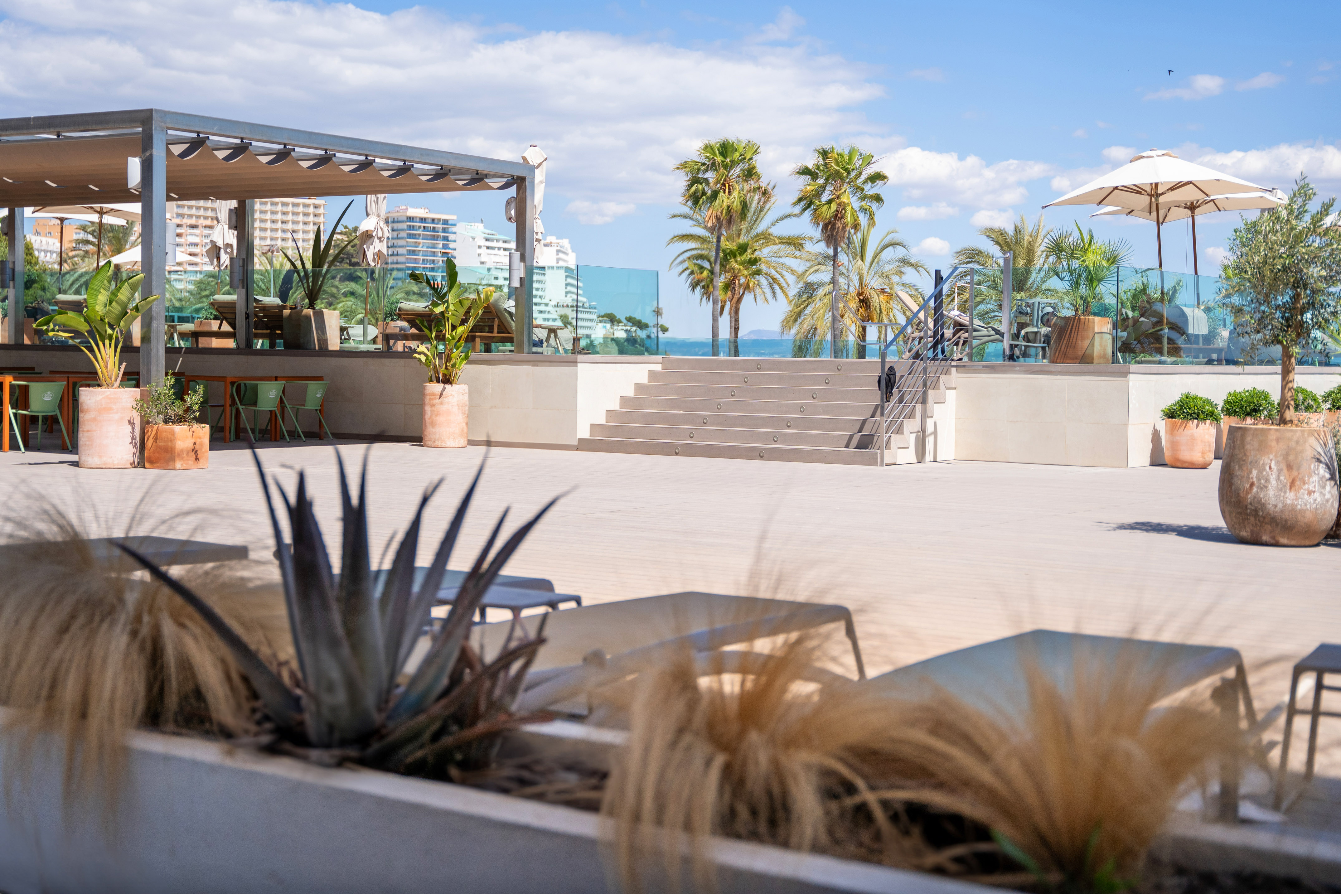 Resort patio with modern pergola, outdoor dining, palm trees, and sea view.