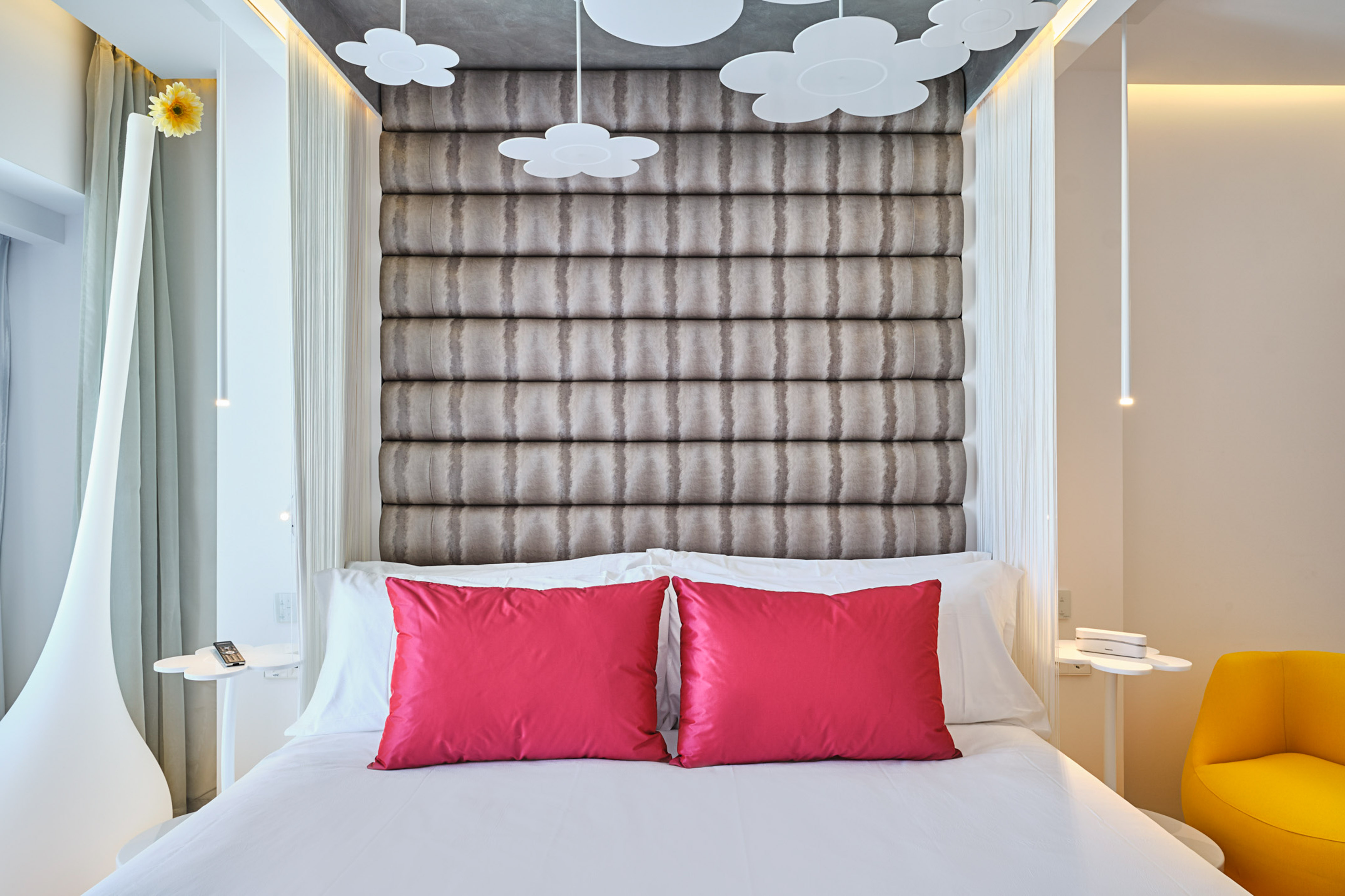 Modern hotel room with white bed, fuchsia pillows, gray headboard, flower ceiling.