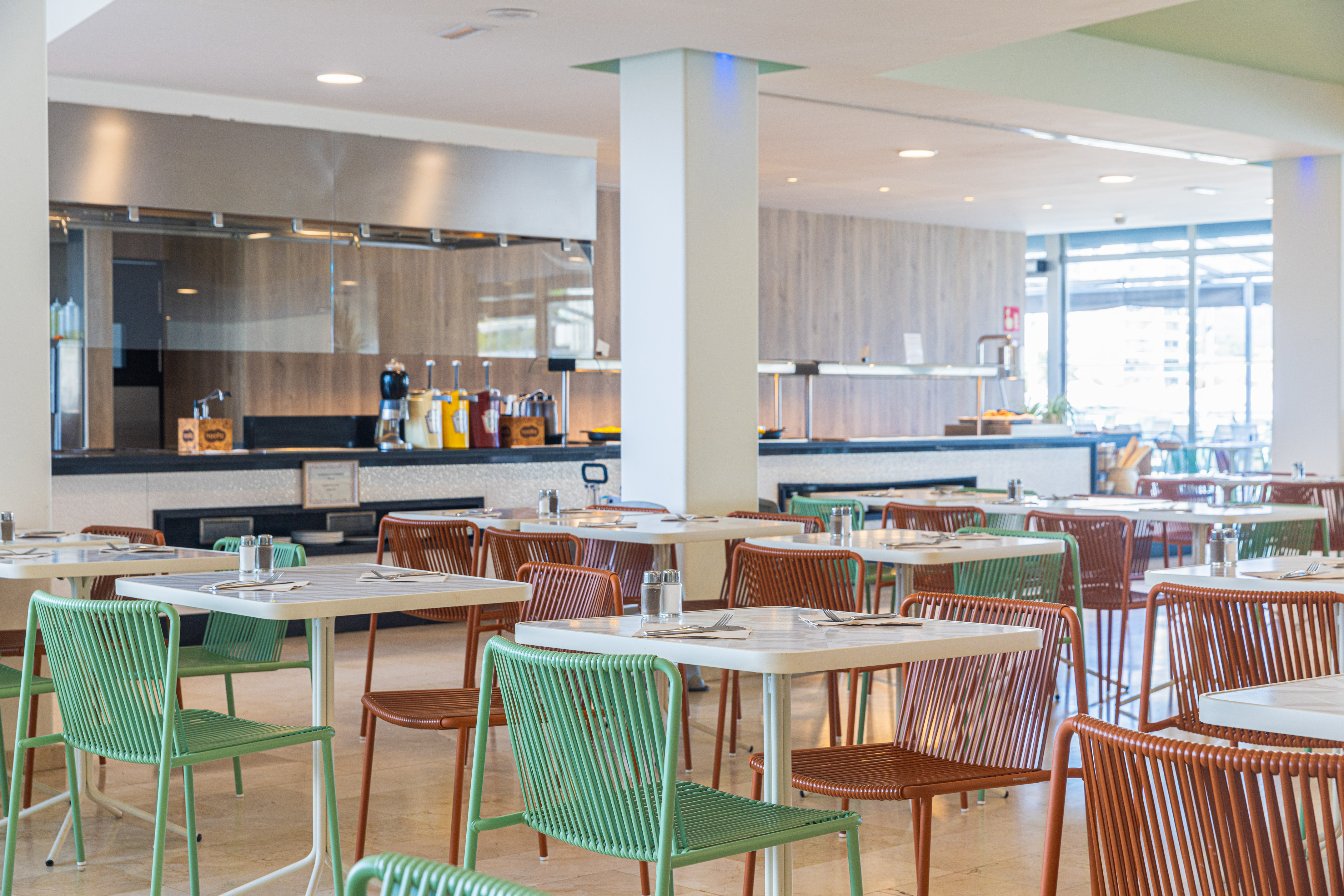 Modern restaurant buffet area with green and brown chairs and white tables.