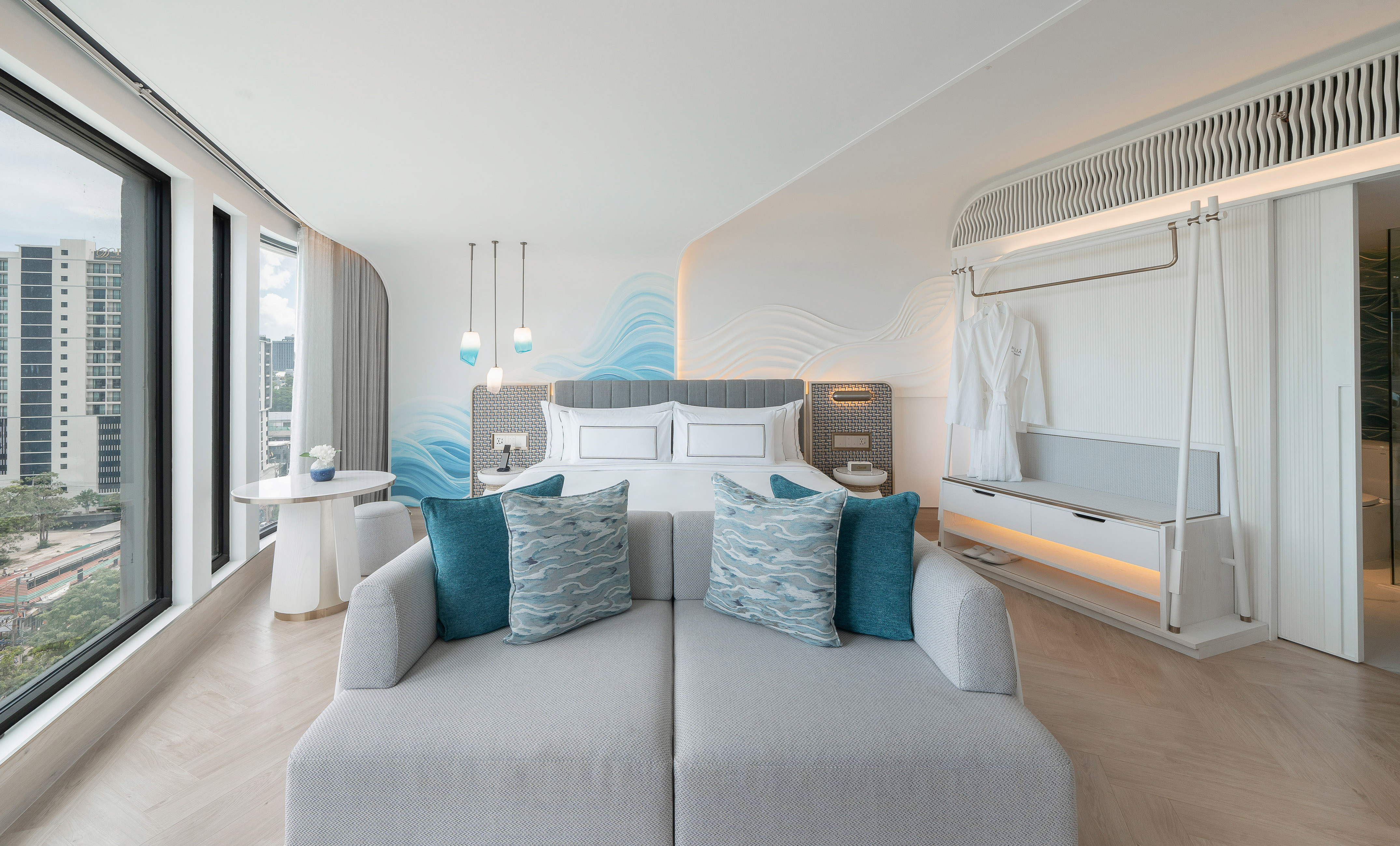 Modern hotel suite with king bed, sofa, city view, and wave wall decor.