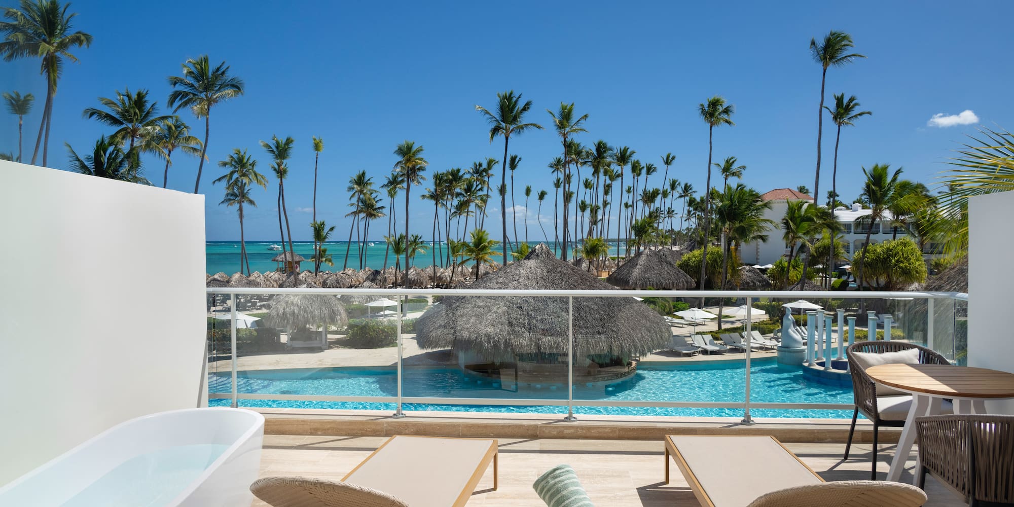 Oceanfront resort balcony with private tub, pool, and tropical palms.