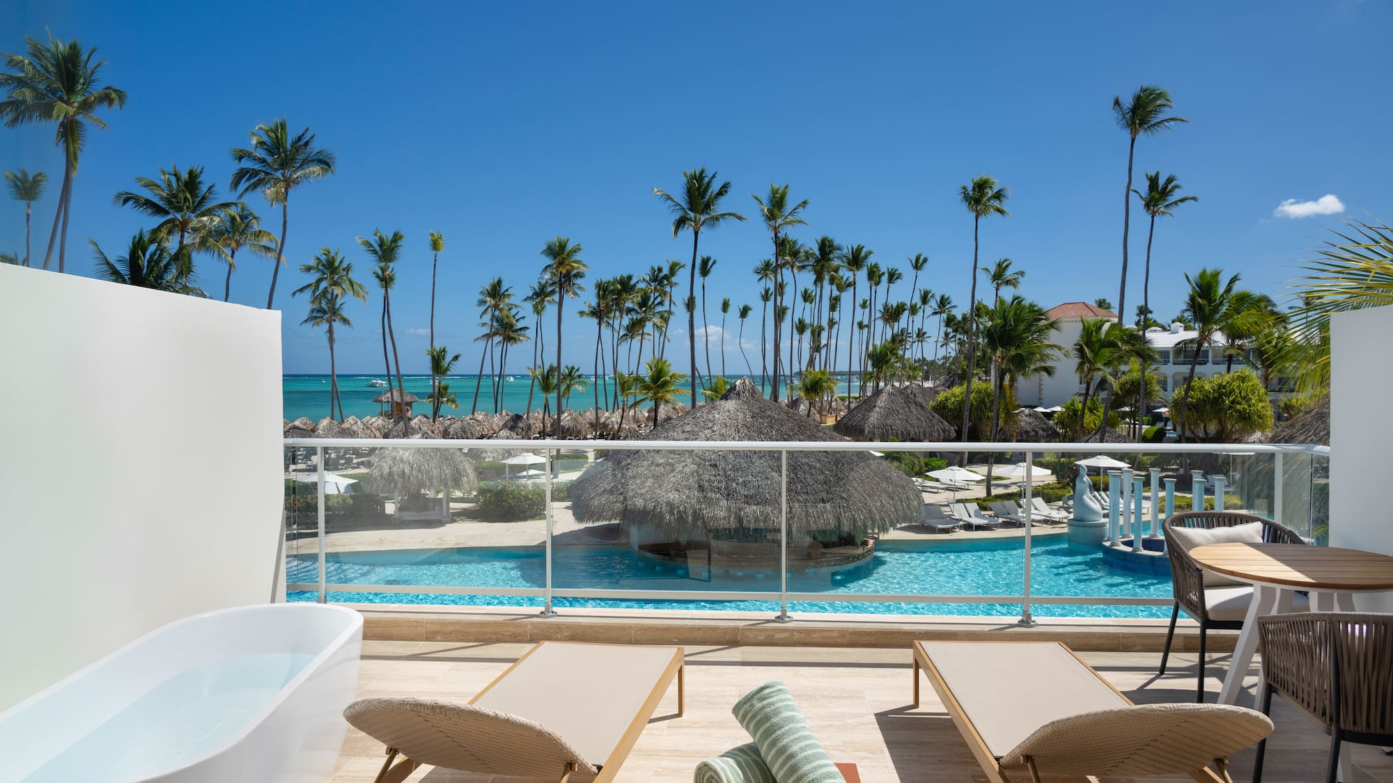 Oceanfront resort balcony with private tub, pool, and tropical palms.