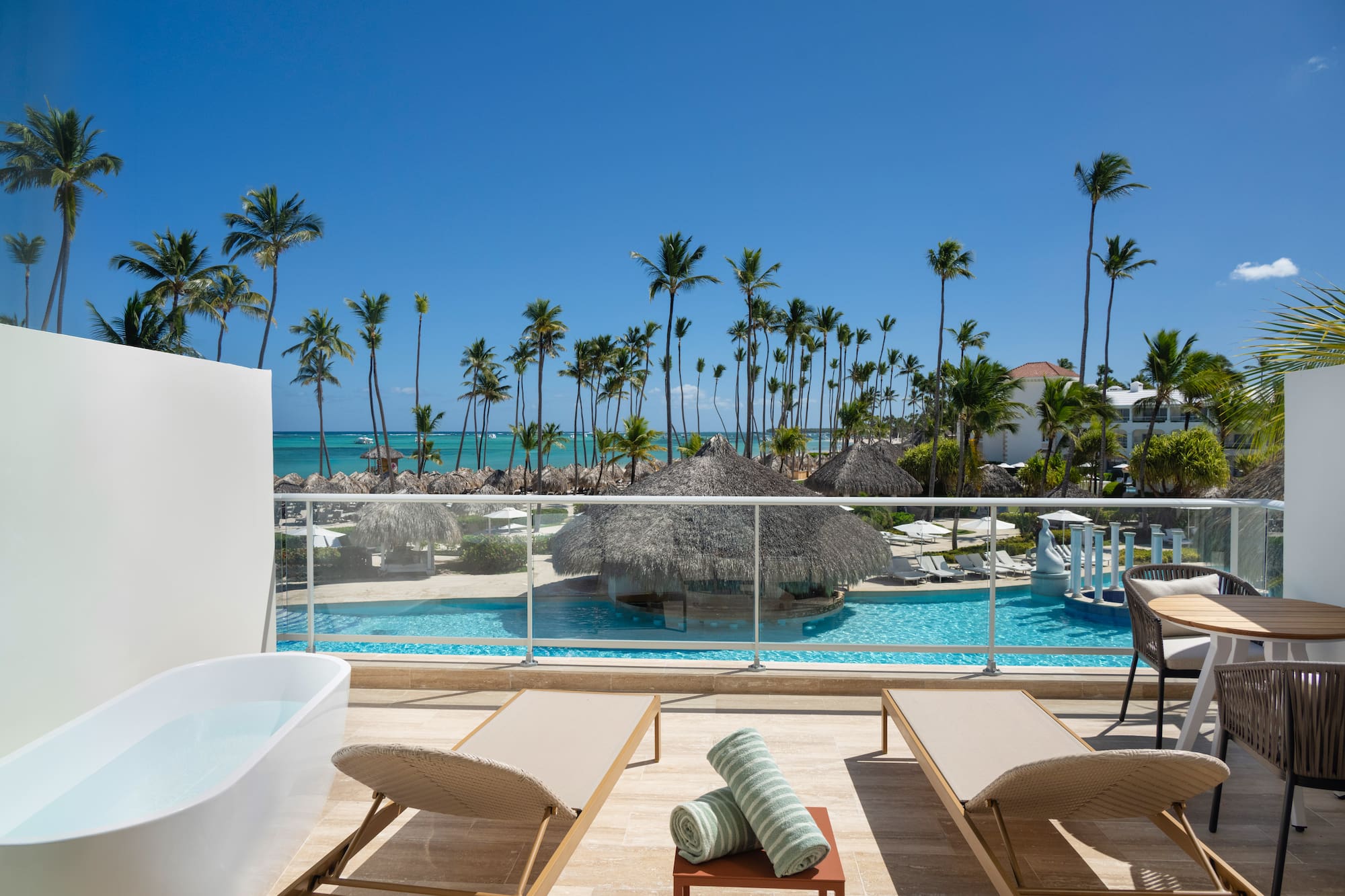 Oceanfront resort balcony with private tub, pool, and tropical palms.