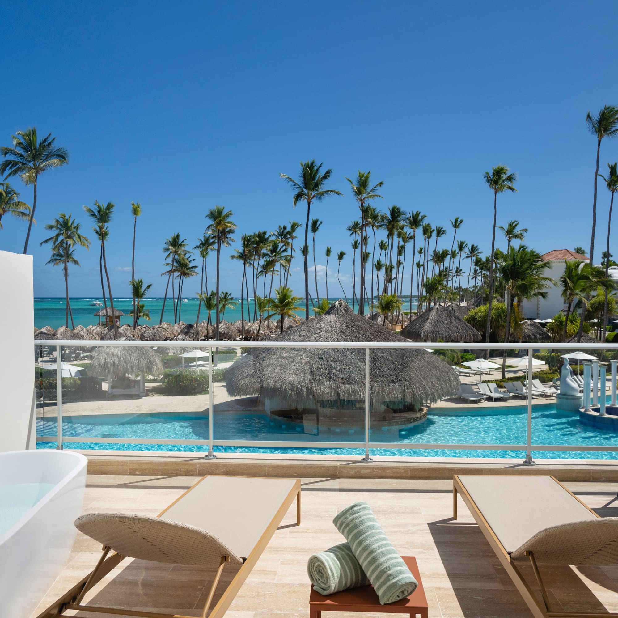 Oceanfront resort balcony with private tub, pool, and tropical palms.