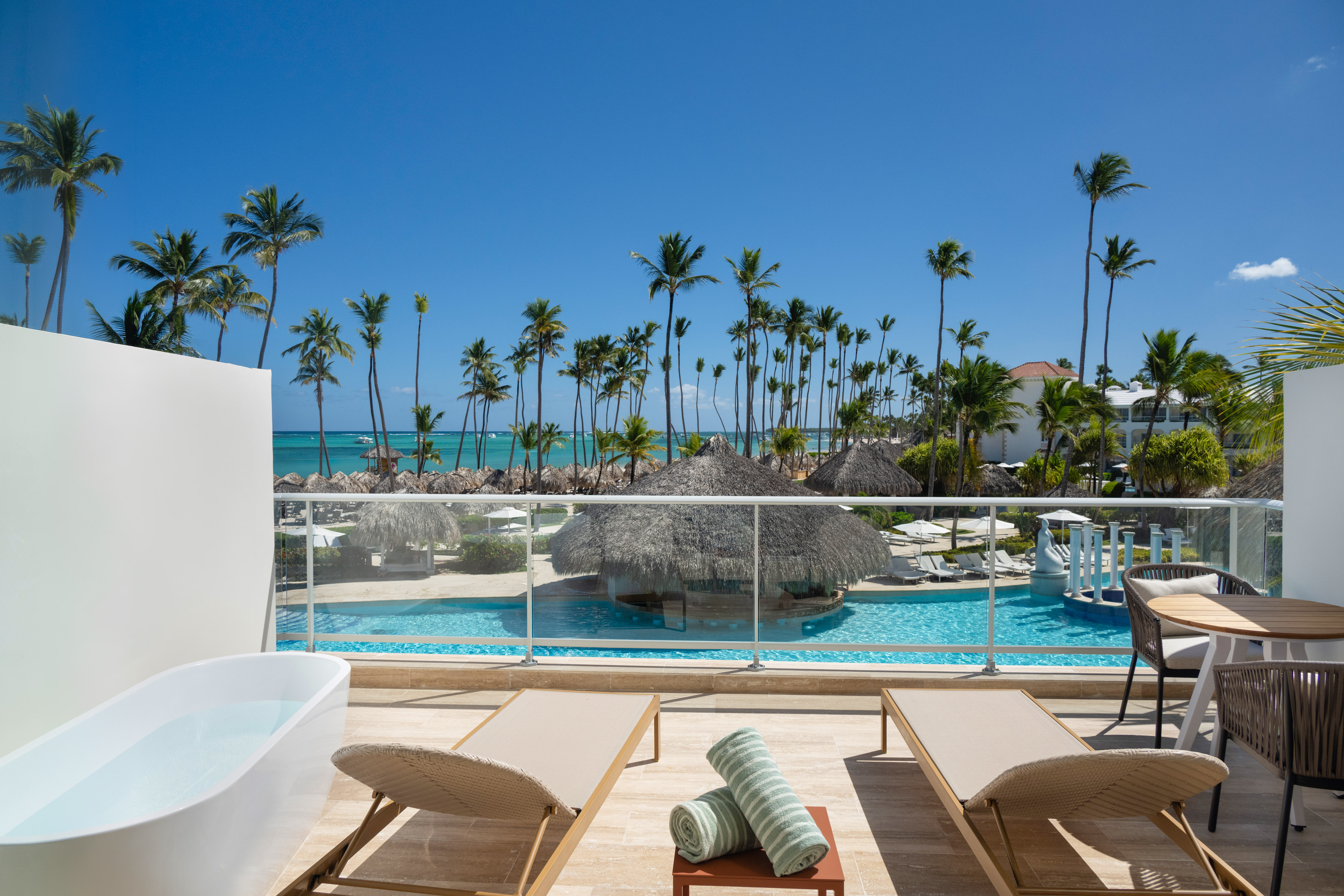 Oceanfront resort balcony with private tub, pool, and tropical palms.